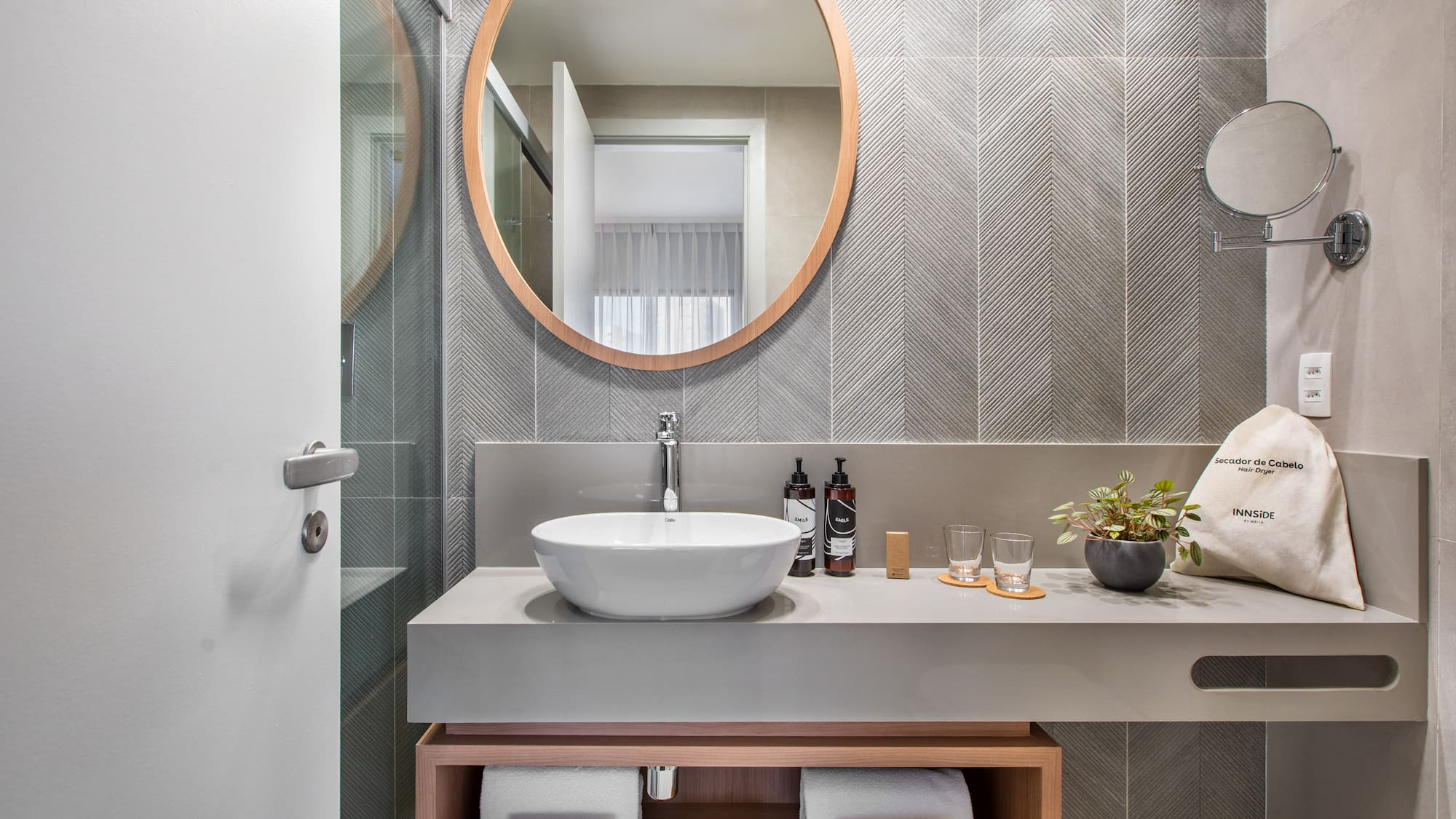 Modern hotel bathroom vanity with wood mirror, vessel sink, gray chevron tiles.