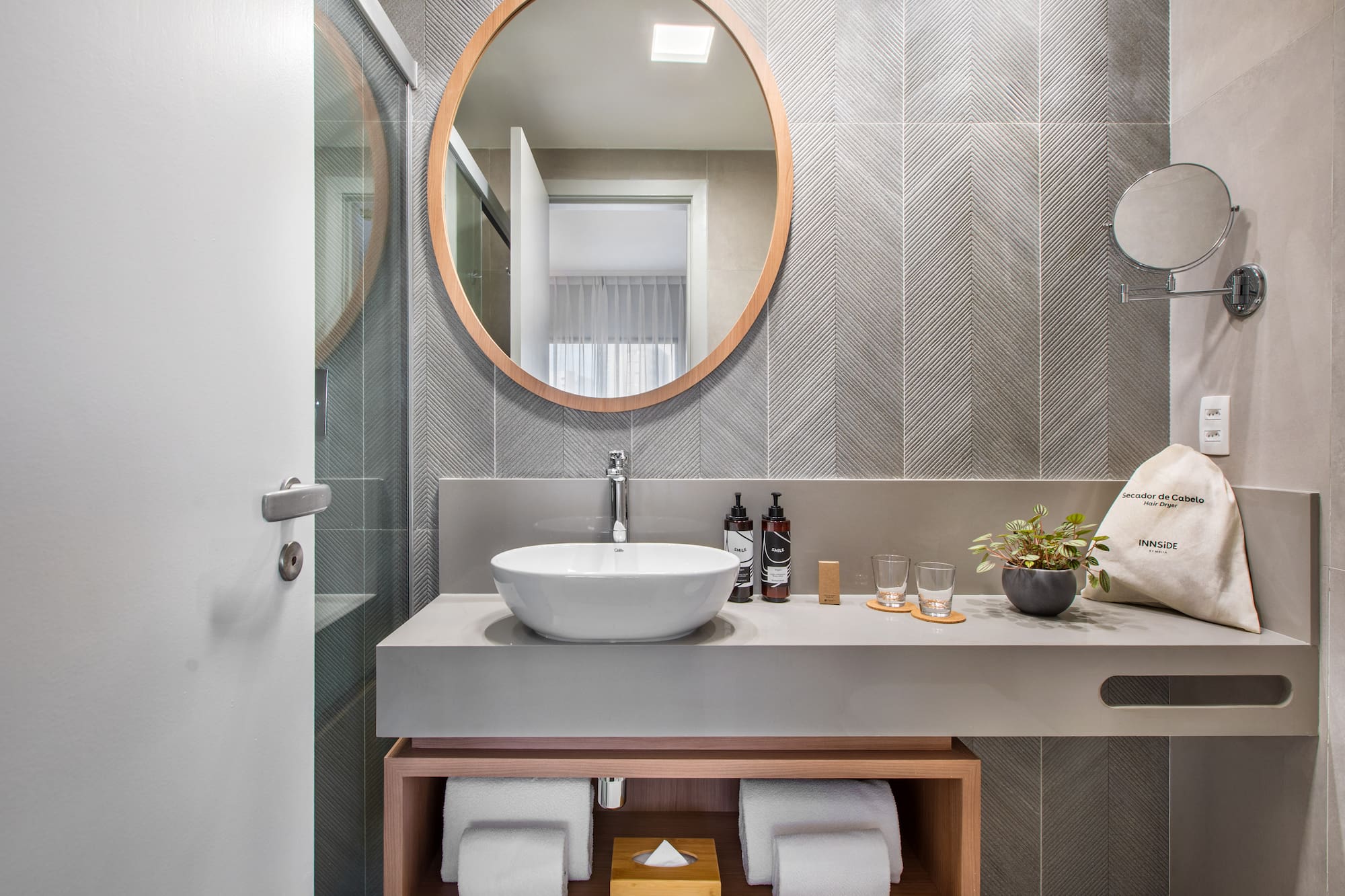 Modern hotel bathroom vanity with wood mirror, vessel sink, gray chevron tiles.