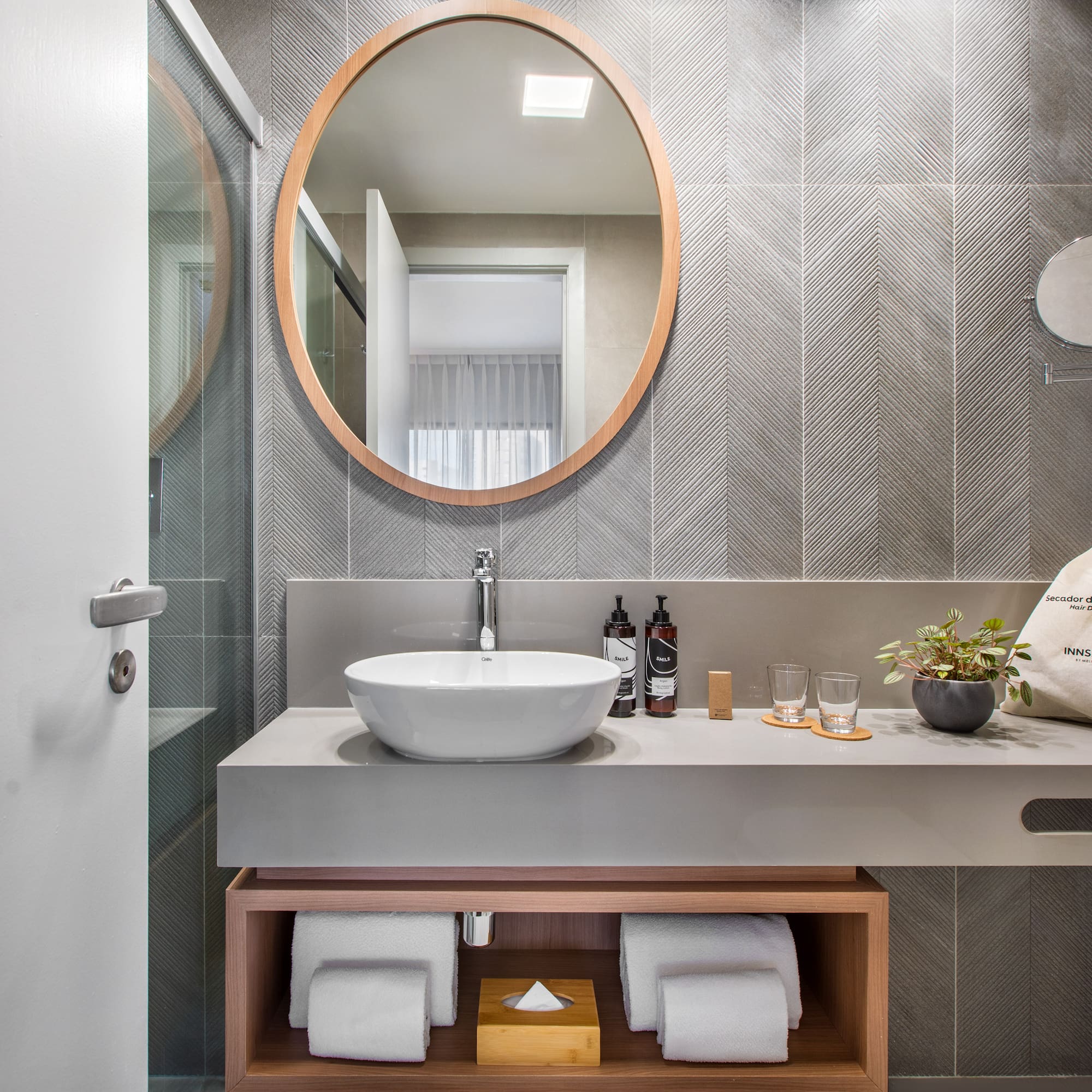 Modern hotel bathroom vanity with wood mirror, vessel sink, gray chevron tiles.