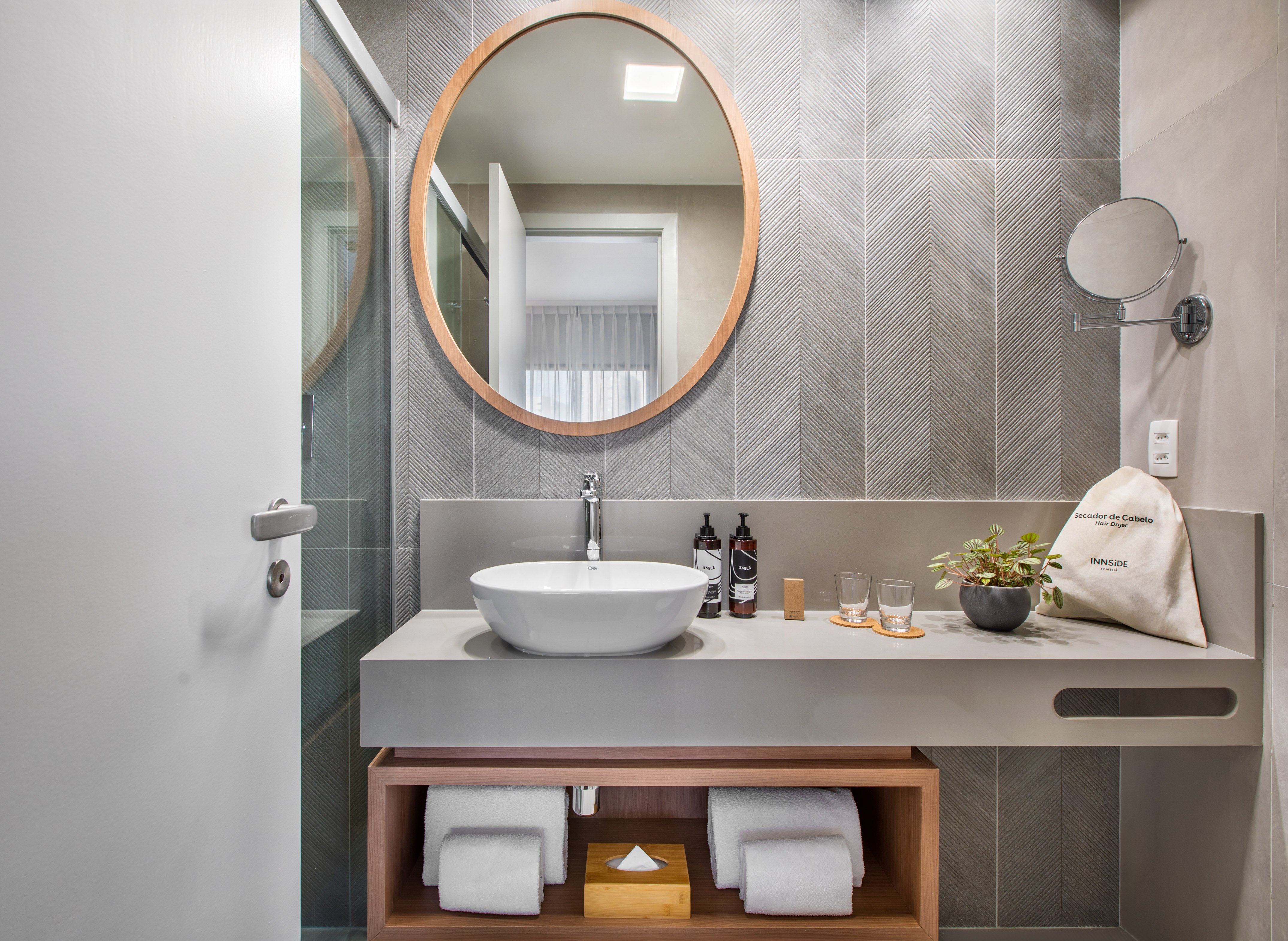 Modern hotel bathroom vanity with wood mirror, vessel sink, gray chevron tiles.