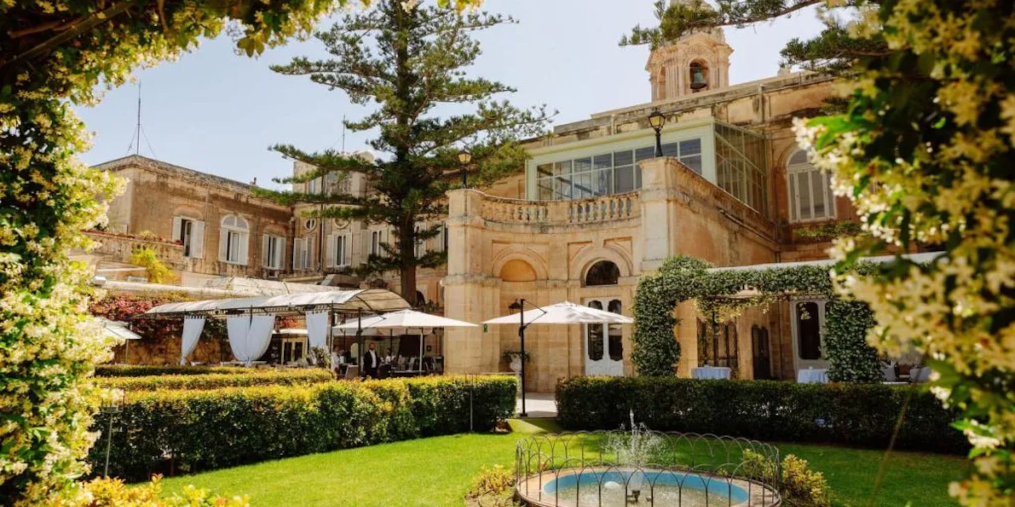 Historic villa garden with fountain, outdoor event setup, and flowering arch.