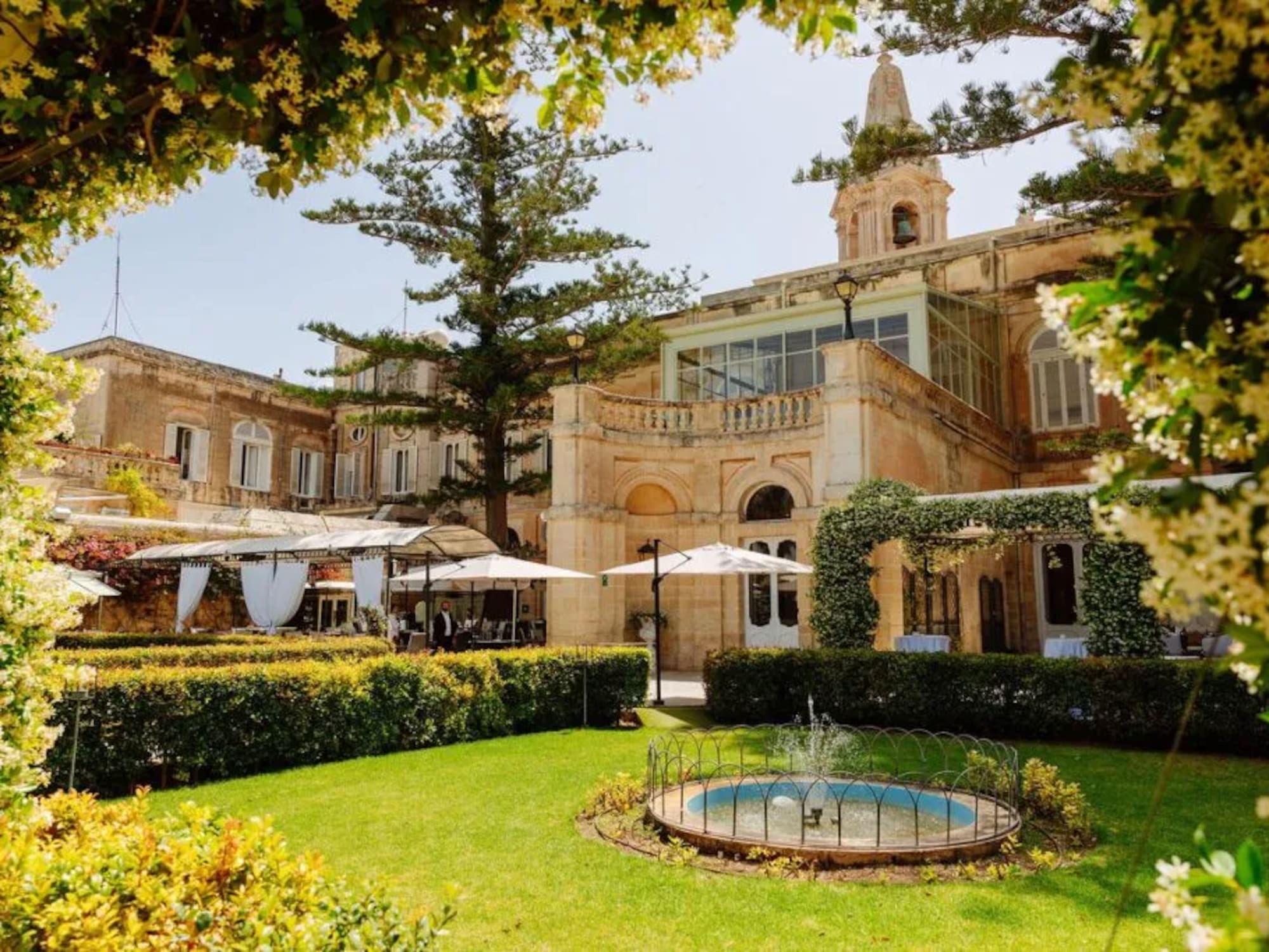 Historic villa garden with fountain, outdoor event setup, and flowering arch.