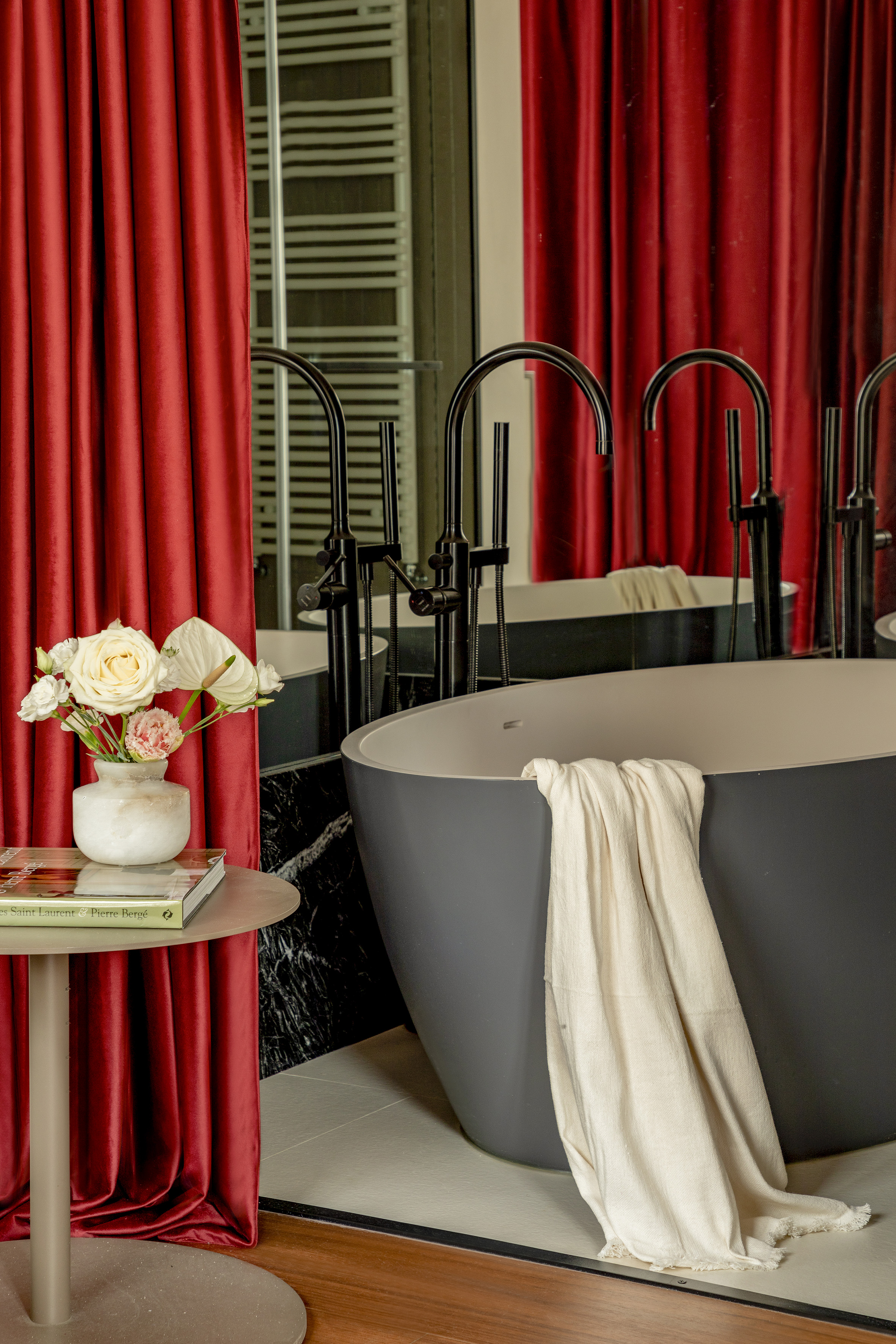Modern bathroom: dark tub, red curtains, black faucets, white flowers.