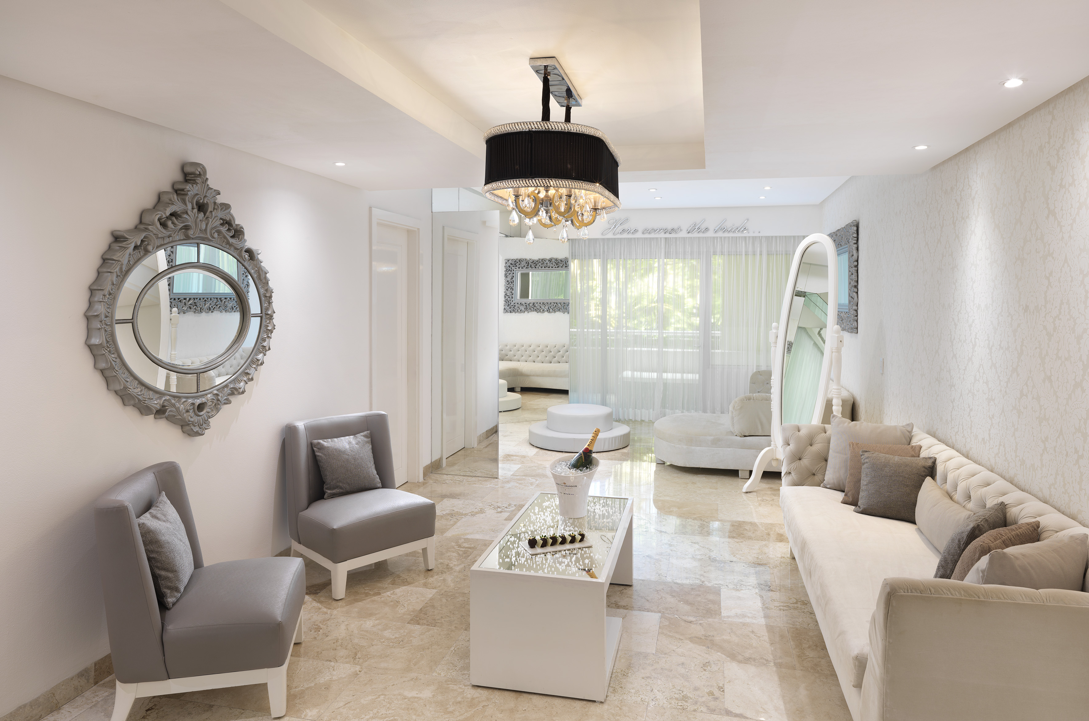 Elegant bridal suite with ornate mirror, white sofa, champagne, and chandelier.
