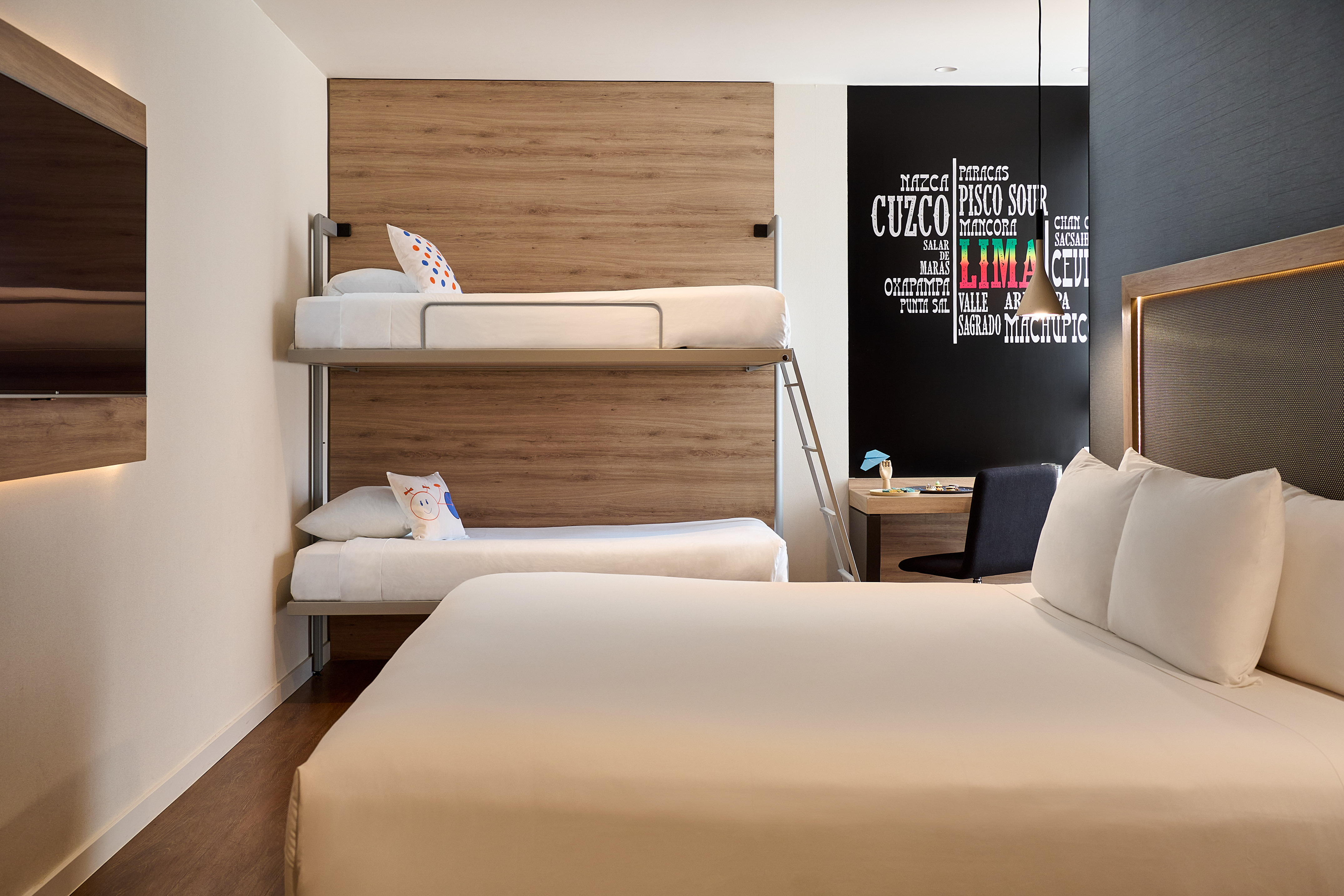 Modern hotel room with queen bed, bunk beds, and Peruvian-themed wall art.