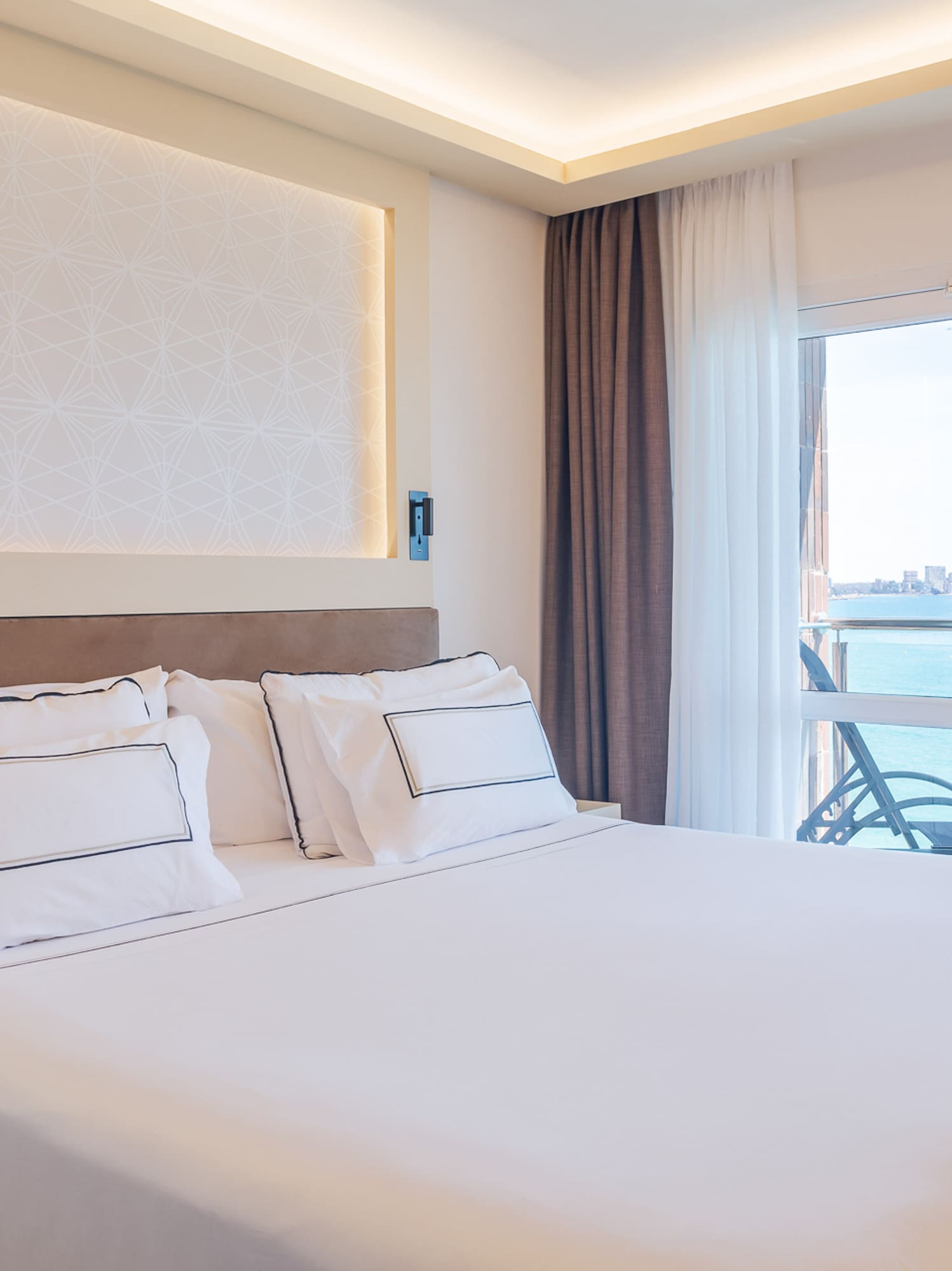 a bed with white sheets and pillows in a room with a glass door