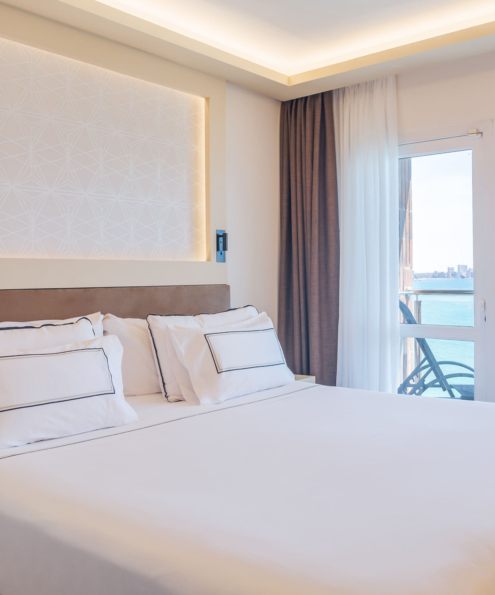 a bed with white sheets and pillows in a room with a glass door