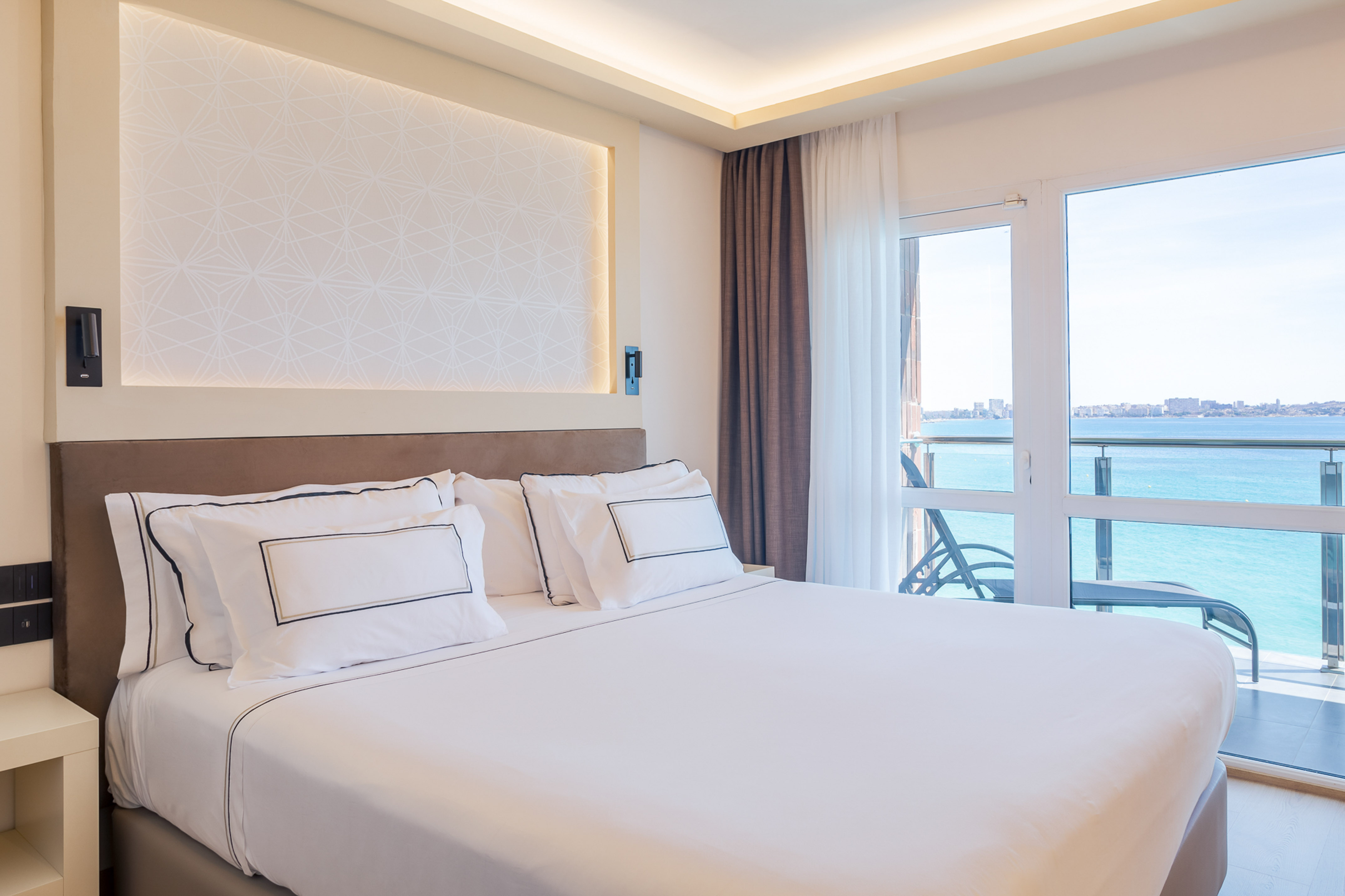 a bed with white sheets and pillows in a room with a glass door