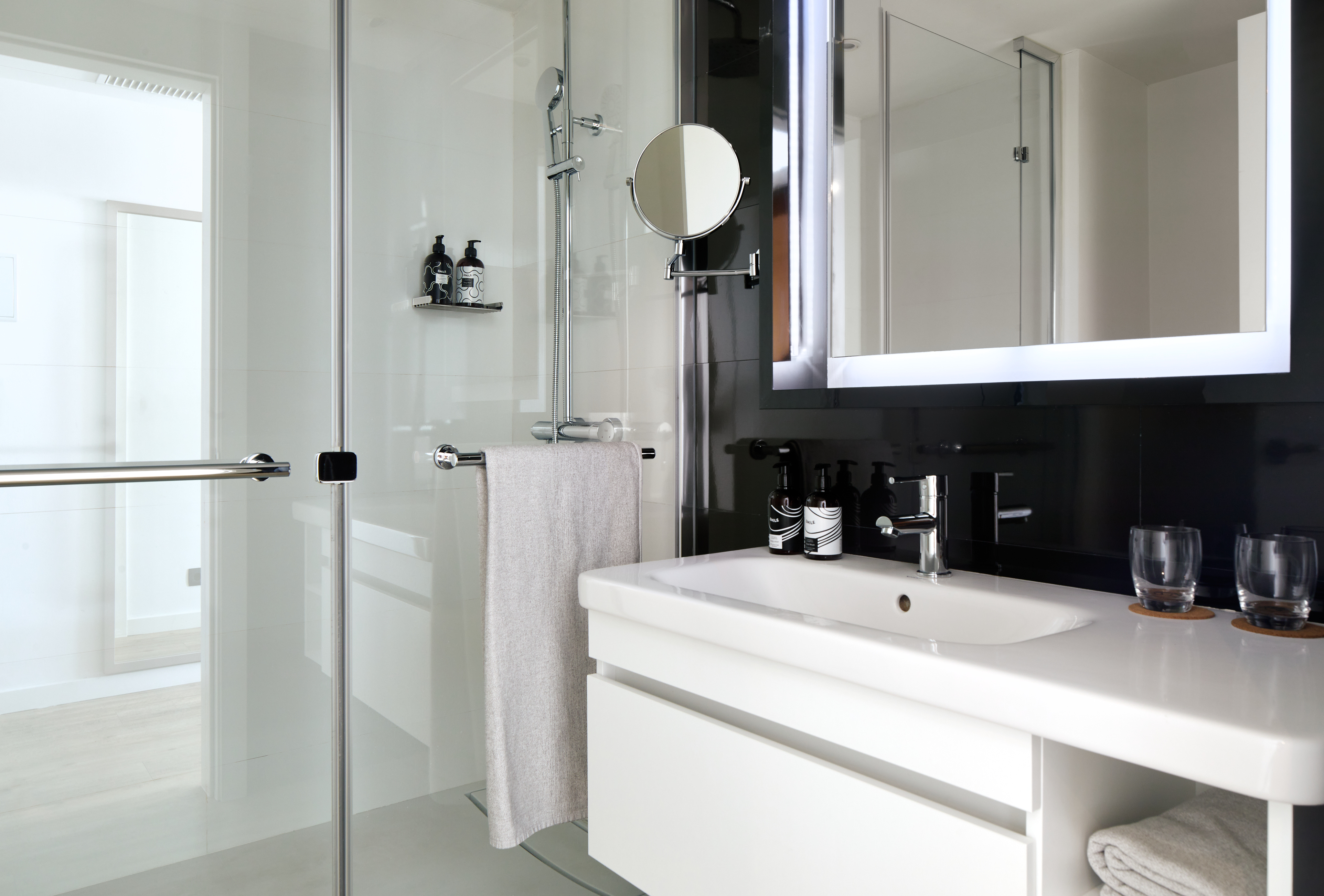 Modern black and white bathroom with glass shower, sink vanity, and backlit mirror.