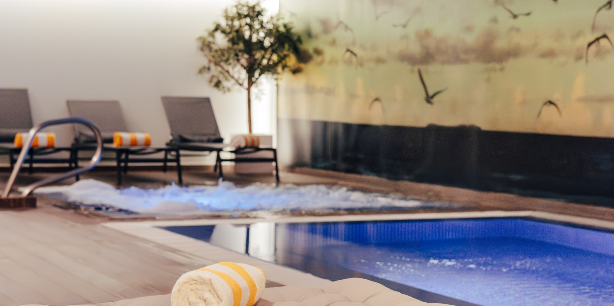 Indoor spa pool with lounge chairs, striped towels, and jacuzzi.