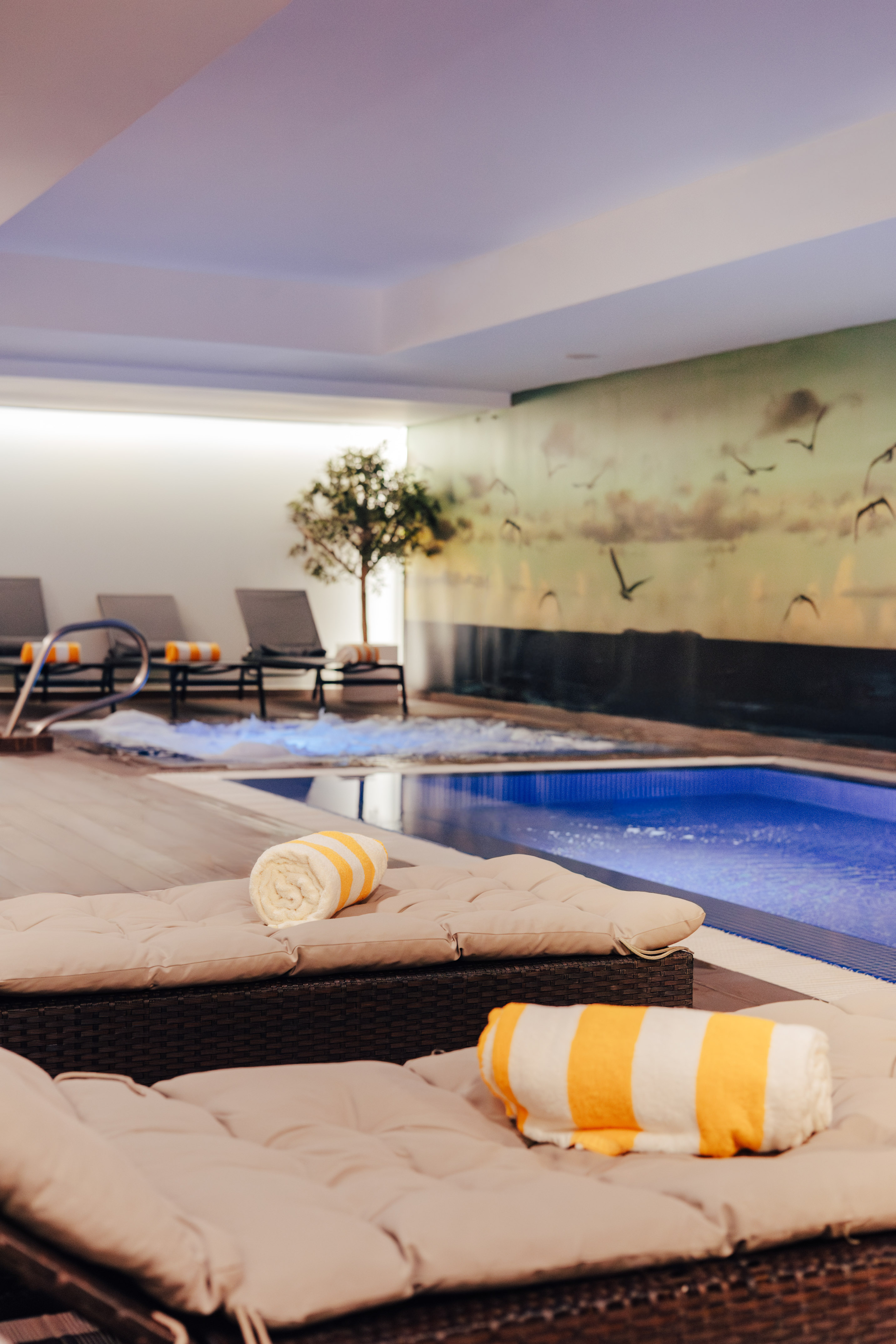 Indoor spa pool with lounge chairs, striped towels, and jacuzzi.