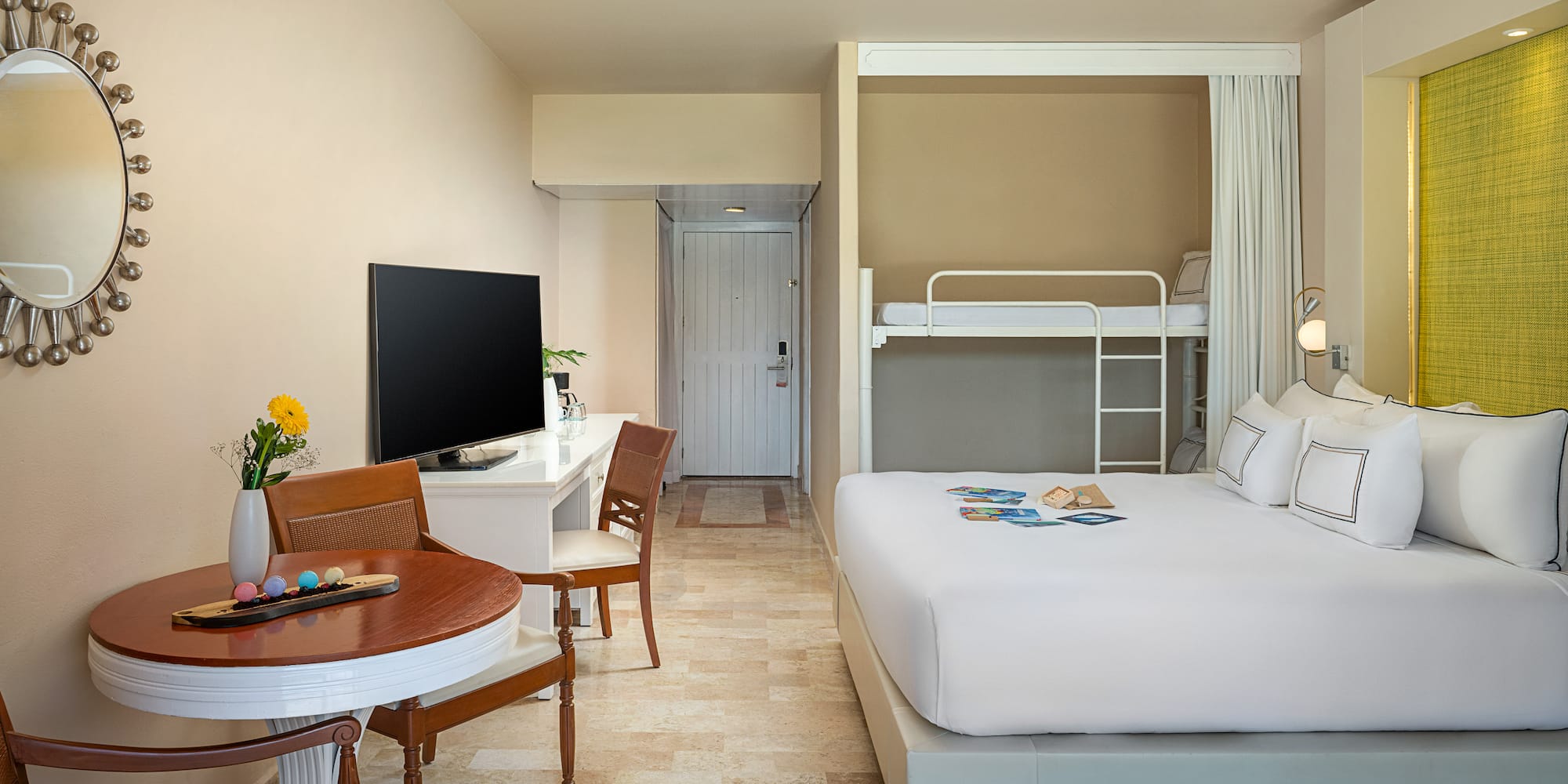 Modern family hotel room with king bed, bunk beds, desk, TV, and dining area.