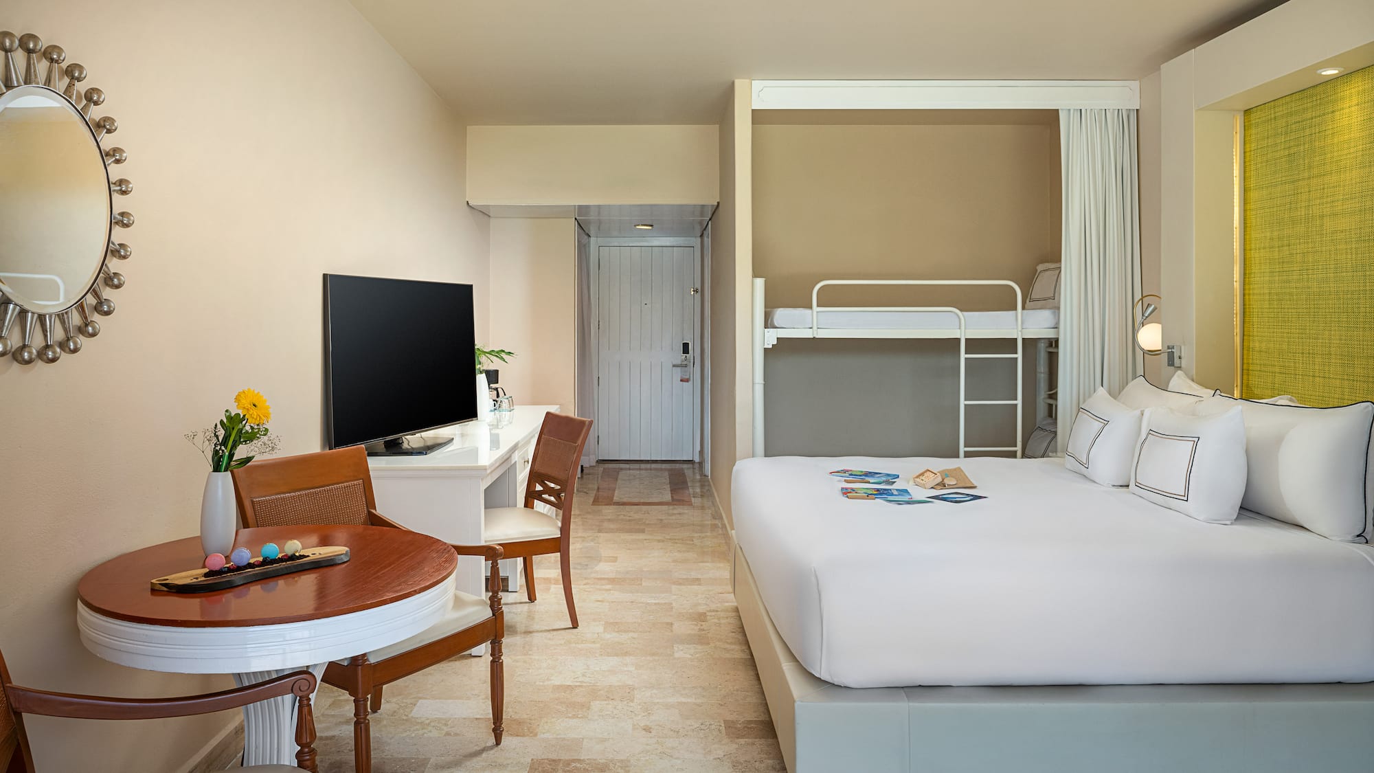 Modern hotel room with large bed, bunk beds, desk, and dining table.