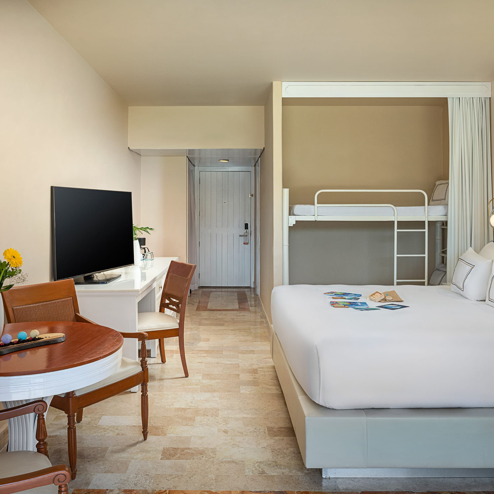 Modern hotel room with large bed, bunk beds, desk, and dining table.