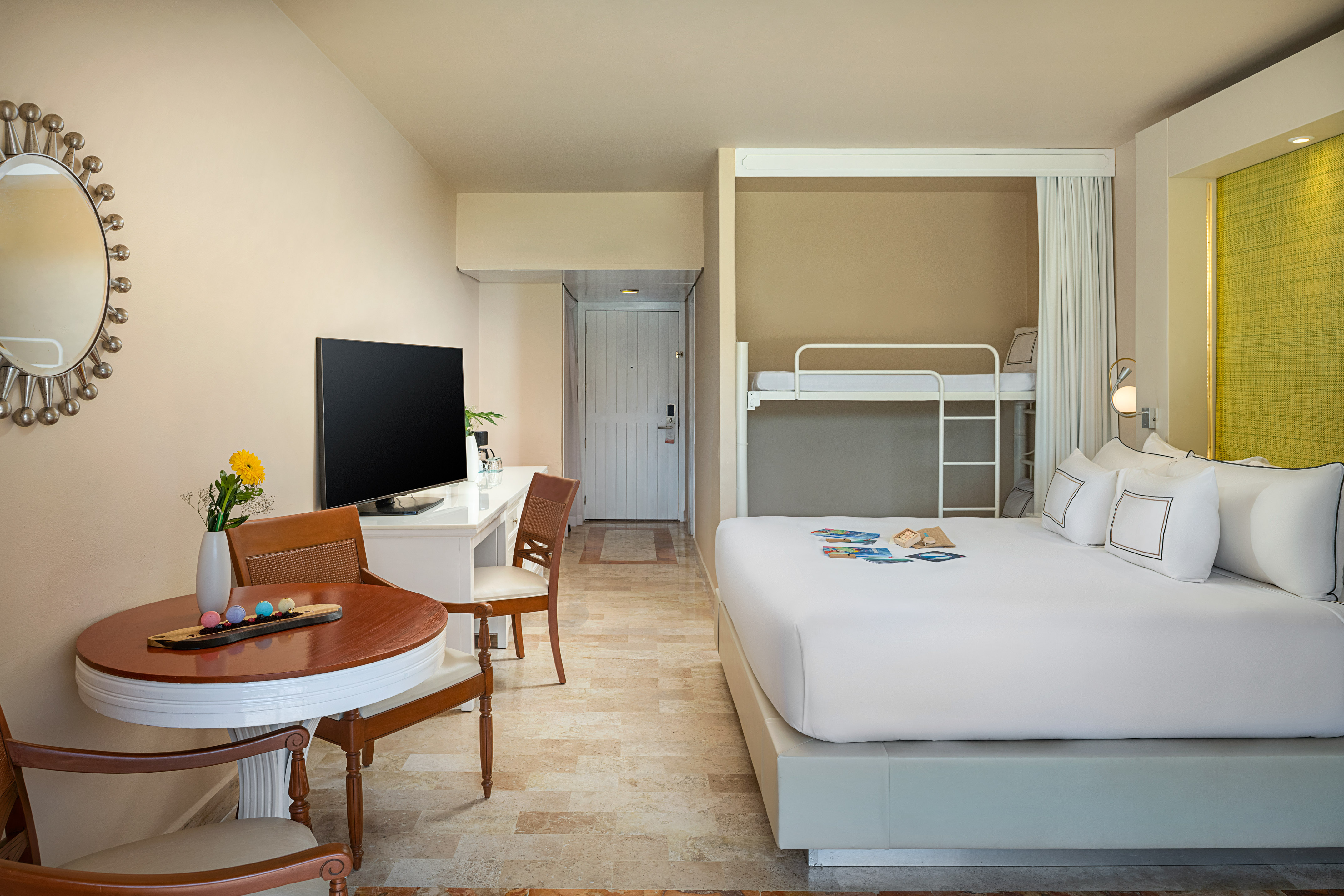 Modern family hotel room with king bed, bunk beds, desk, TV, and dining area.