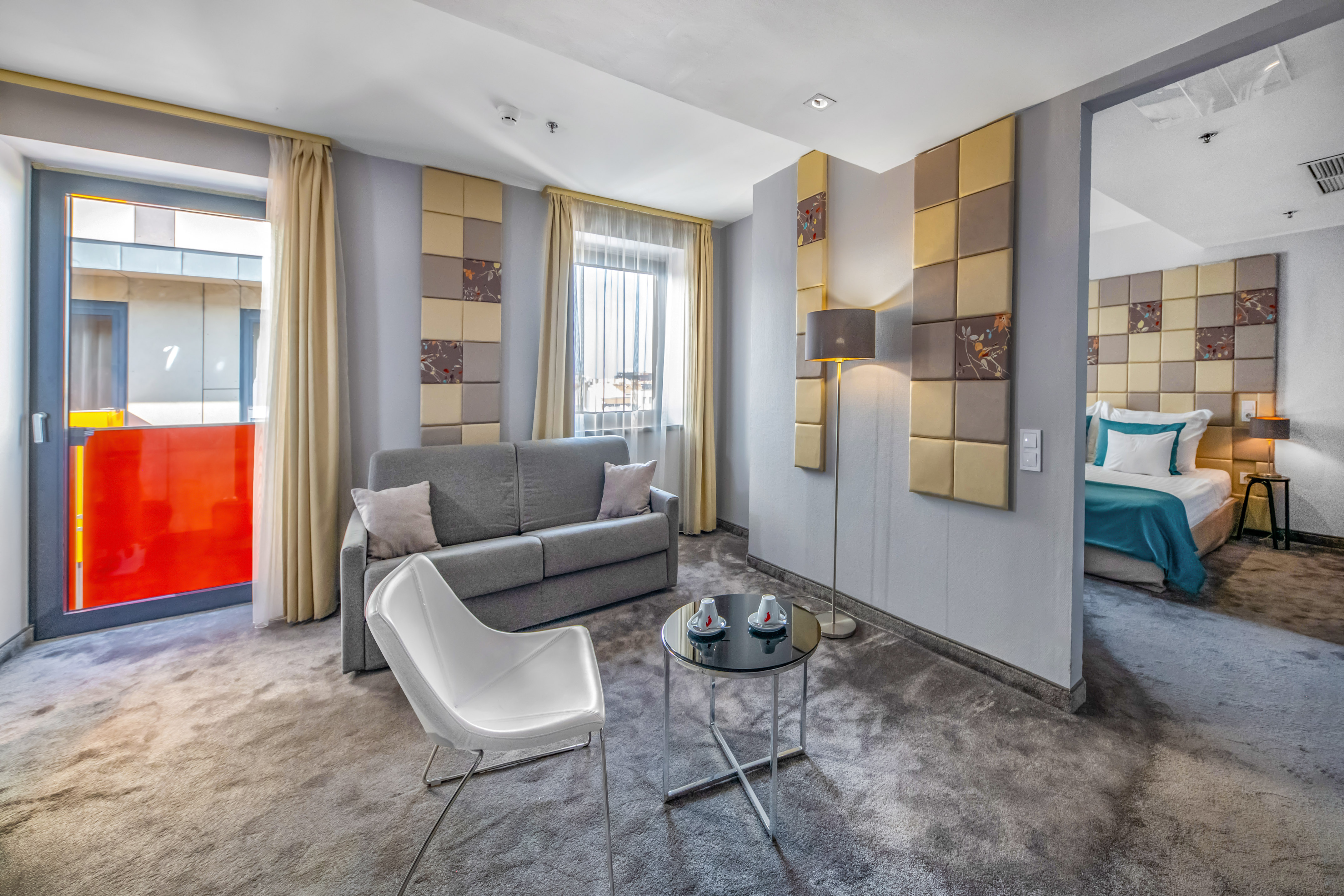 Hotel suite with living room, gray sofa, patterned walls, and adjacent bedroom.