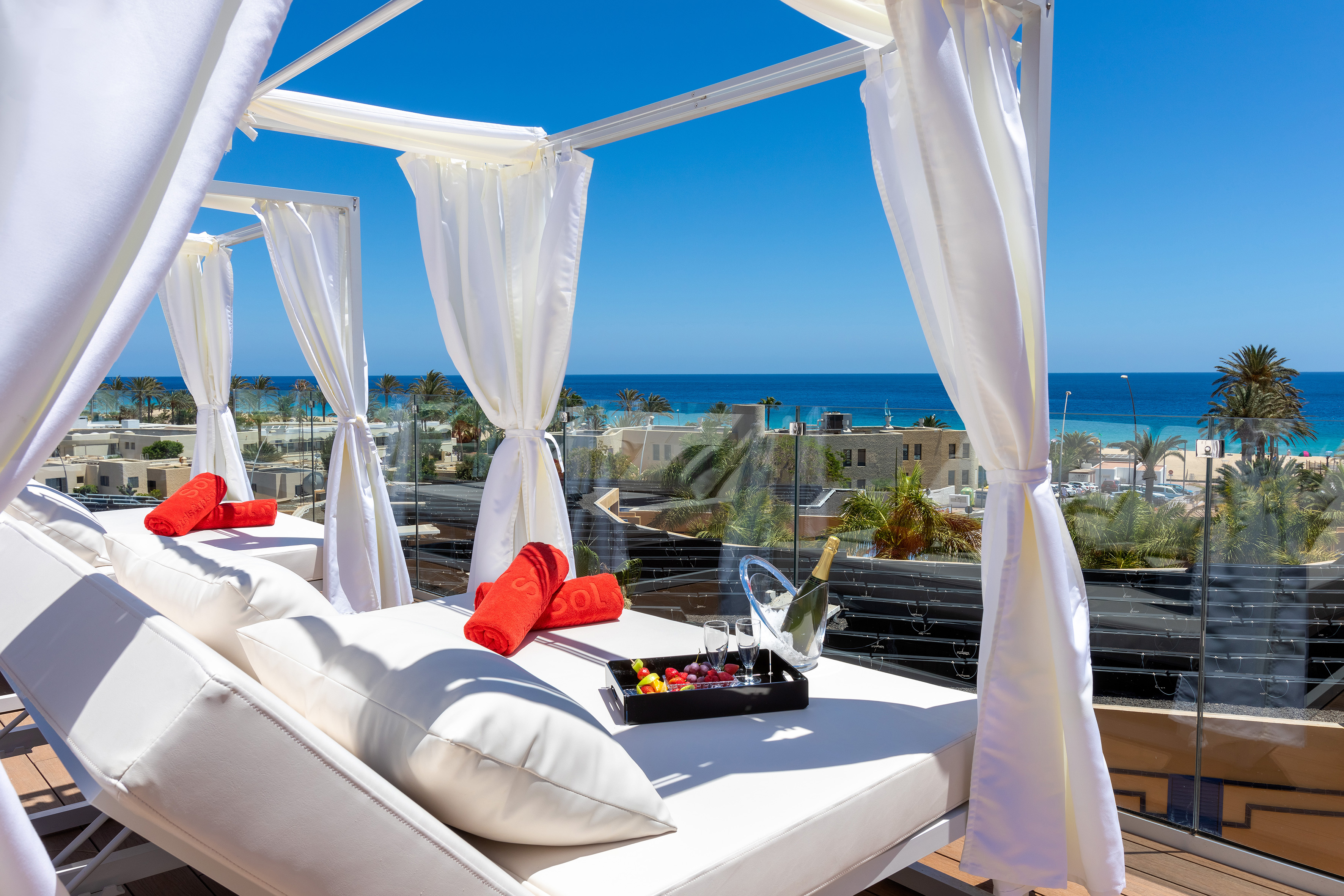 Luxury ocean view daybed with champagne, fruit, and red towels.