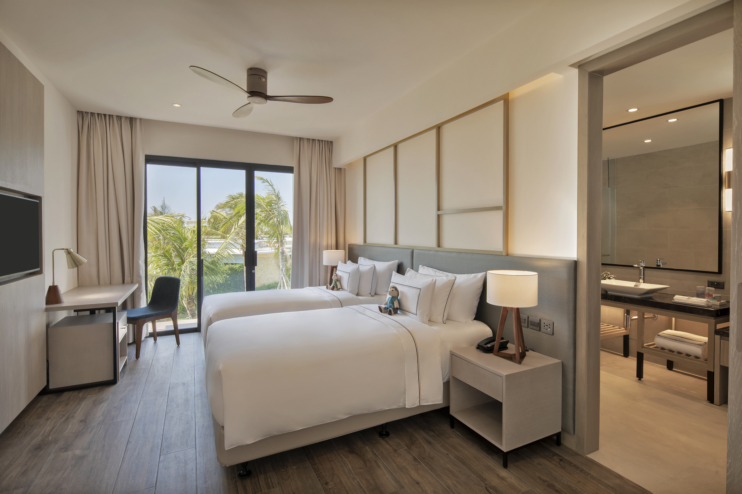 Modern hotel room with twin beds, tropical view, and ensuite bathroom.