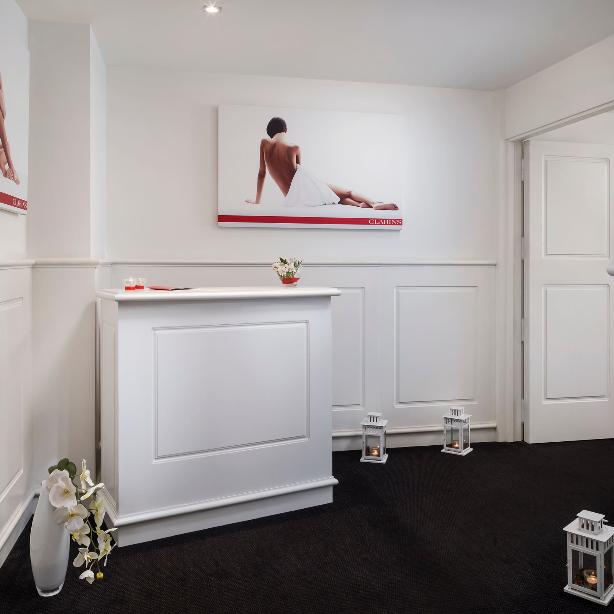 Elegant Clarins spa reception with white desk, skincare posters, and candles.