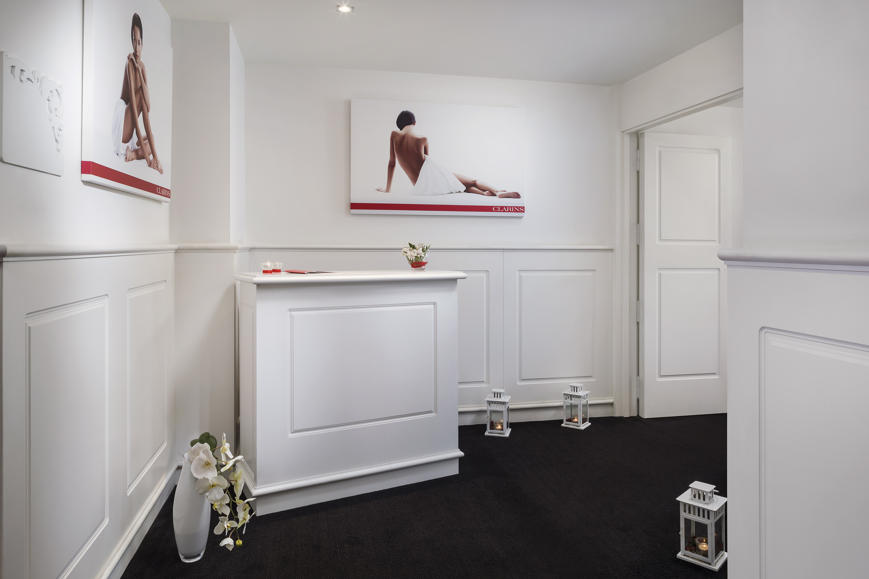Elegant Clarins spa reception with white desk, skincare posters, and candles.
