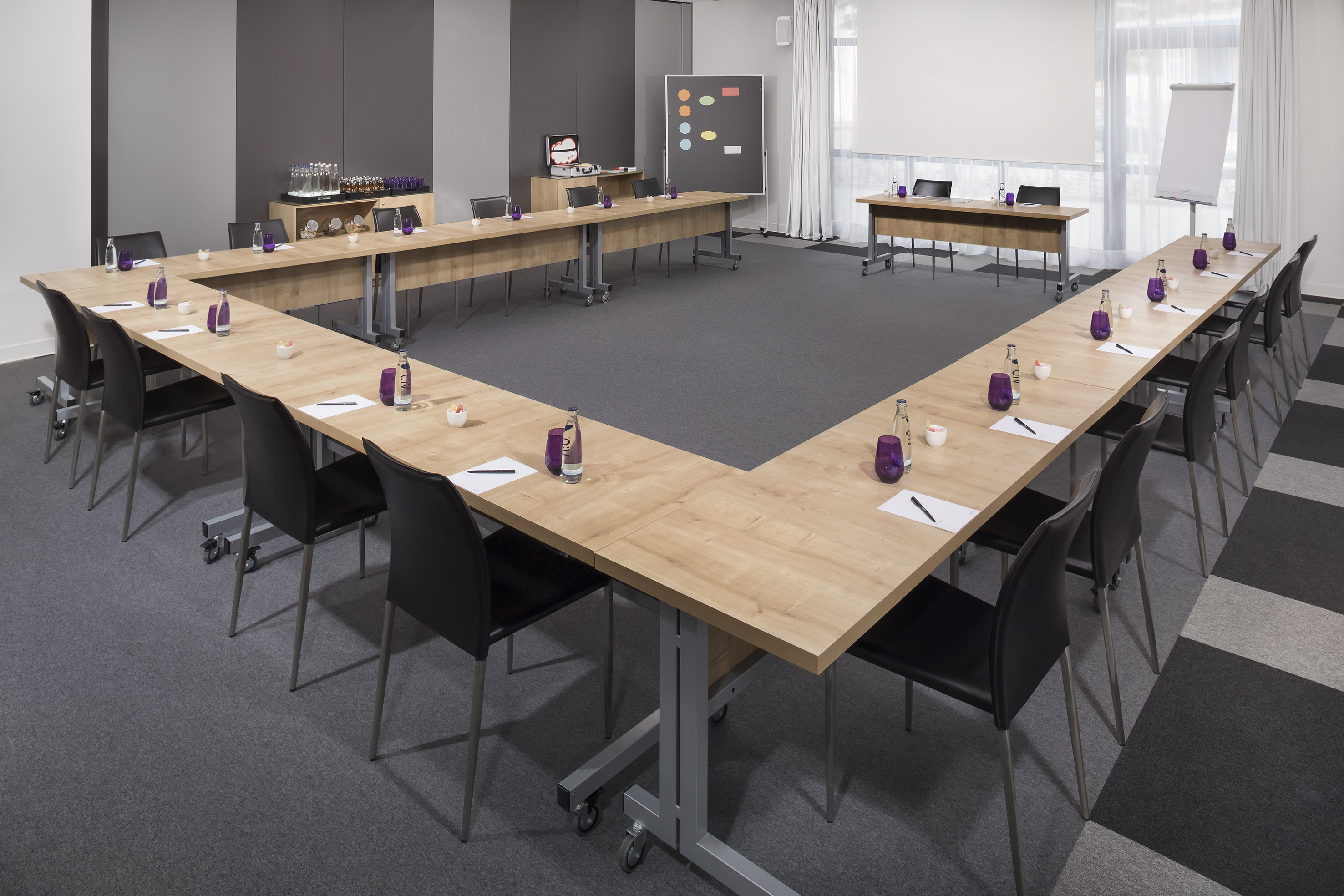 Modern U-shaped meeting room setup with tables, chairs, and presentation screen.