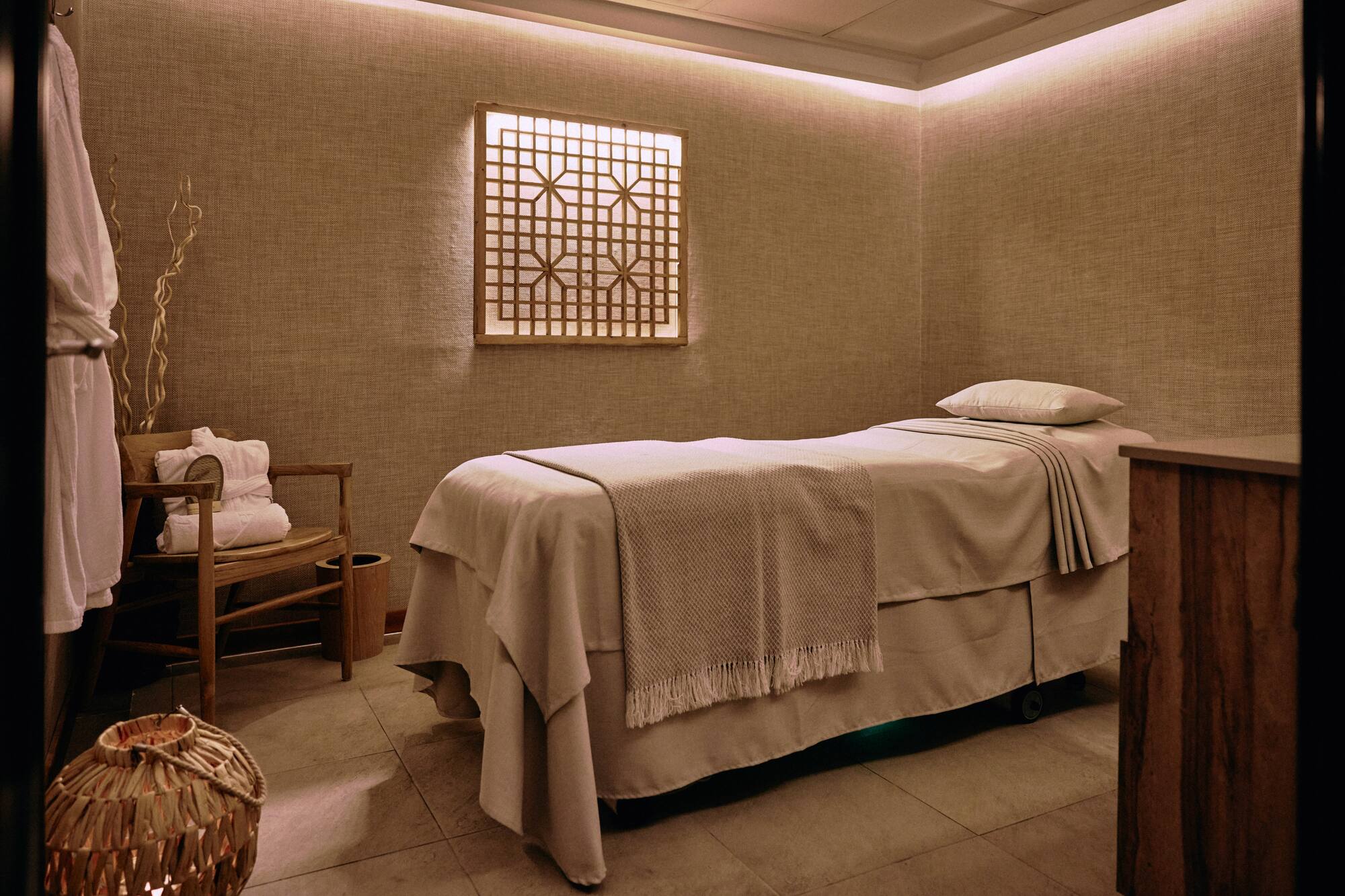 Spa treatment room with massage bed, warm lighting, and Asian-inspired decor.