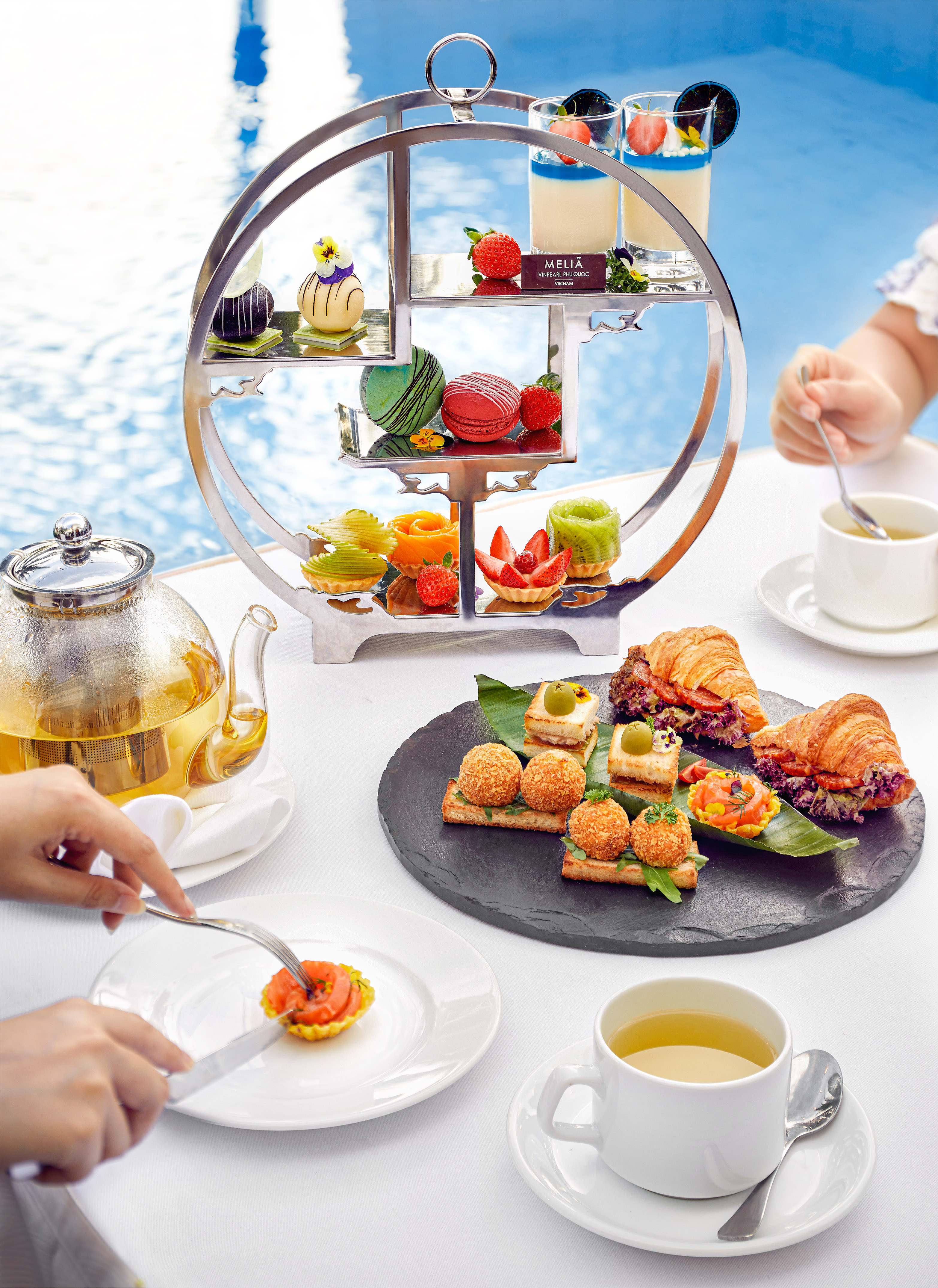 Melia Phu Quoc high tea: tiered desserts, savory bites, and tea by resort pool.