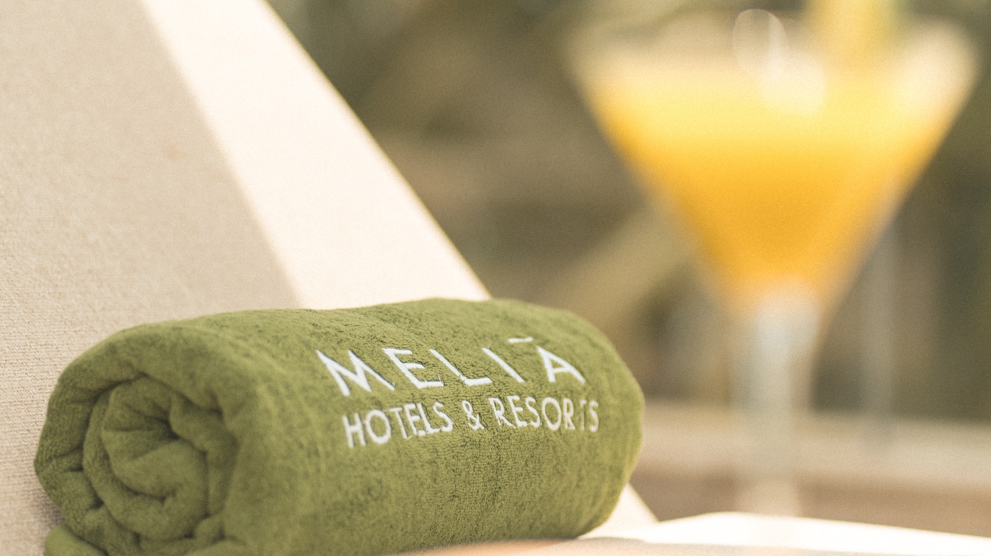 Green Melia Hotels & Resorts towel on lounge chair with blurred cocktail.