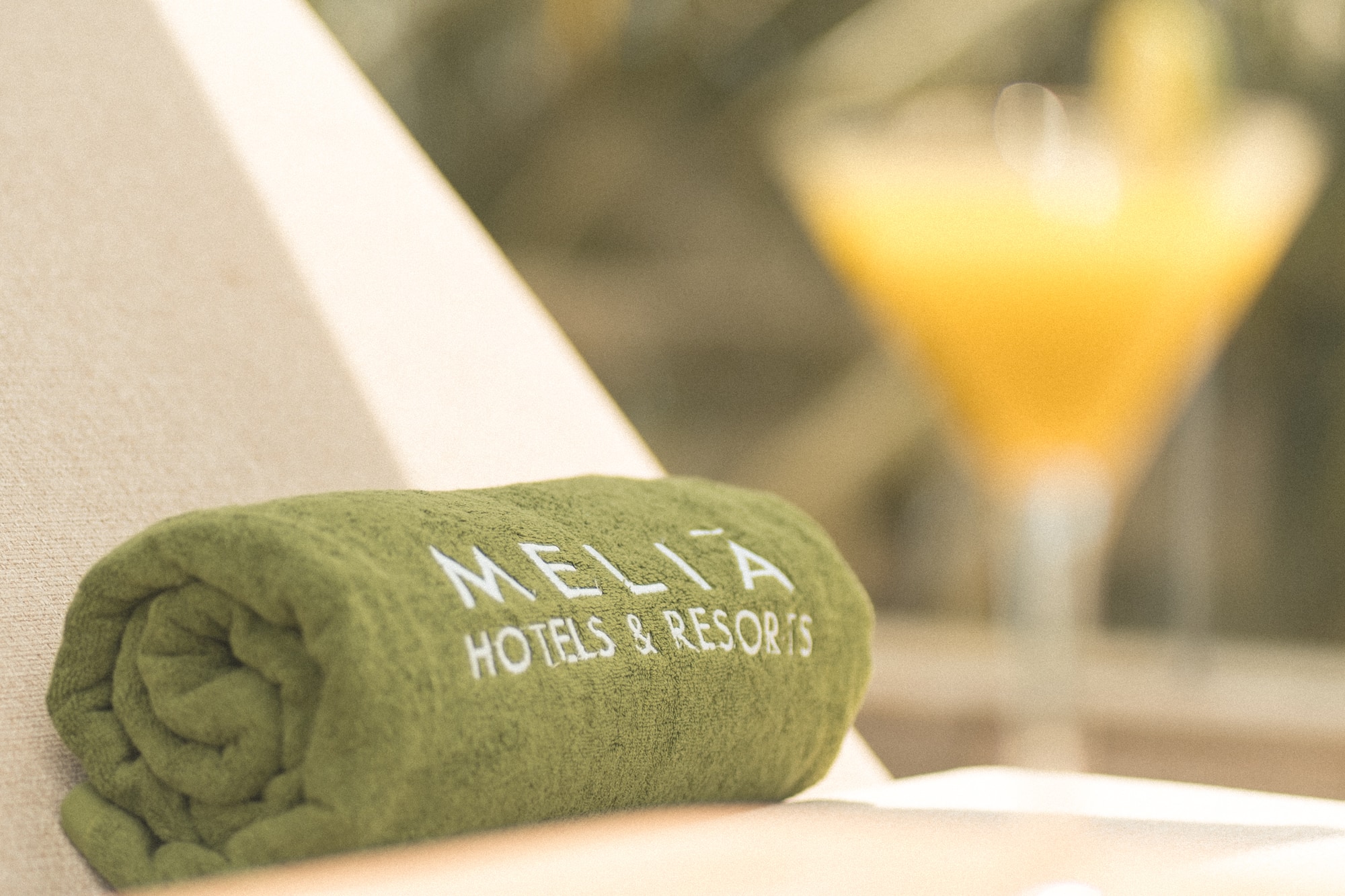Green Melia Hotels & Resorts towel on lounge chair with blurred cocktail.