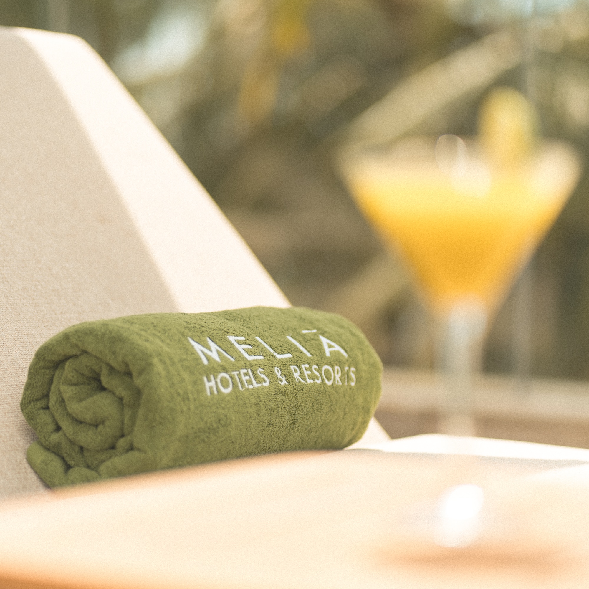 Green Melia Hotels & Resorts towel on lounge chair with blurred cocktail.