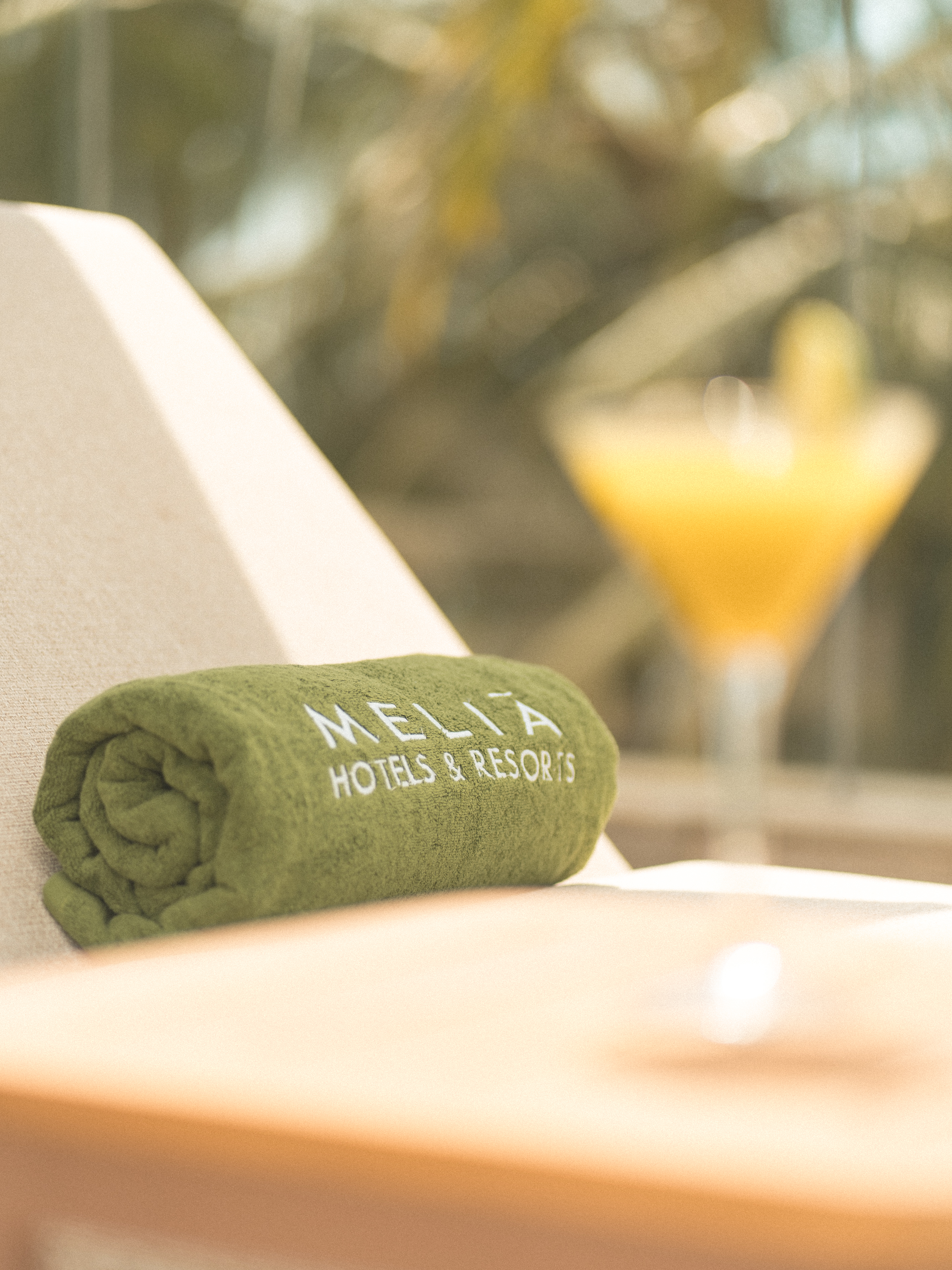 Green Melia Hotels & Resorts towel on lounge chair with blurred cocktail.