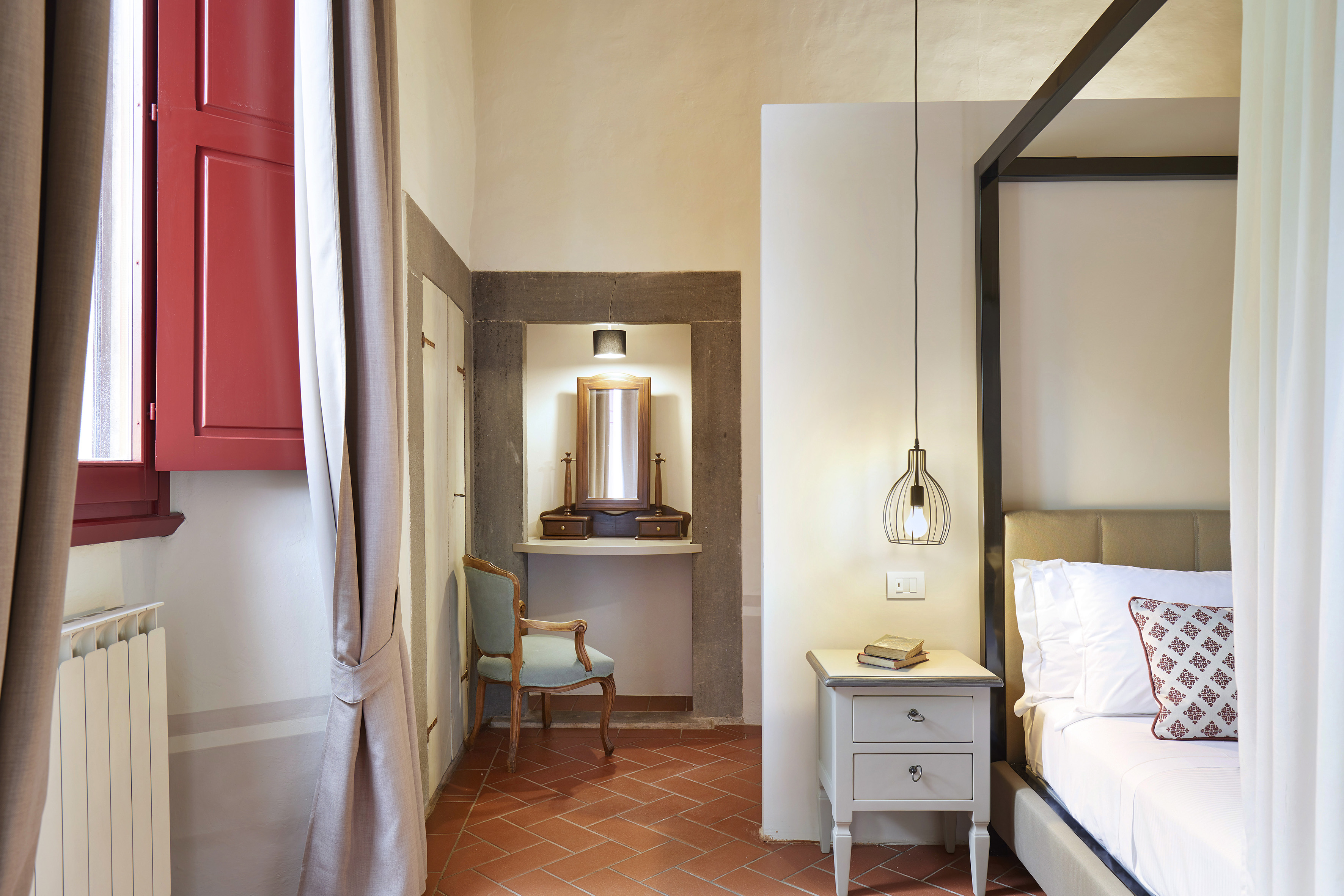 Four-poster bed, red shutters, terracotta floor bedroom with vanity.