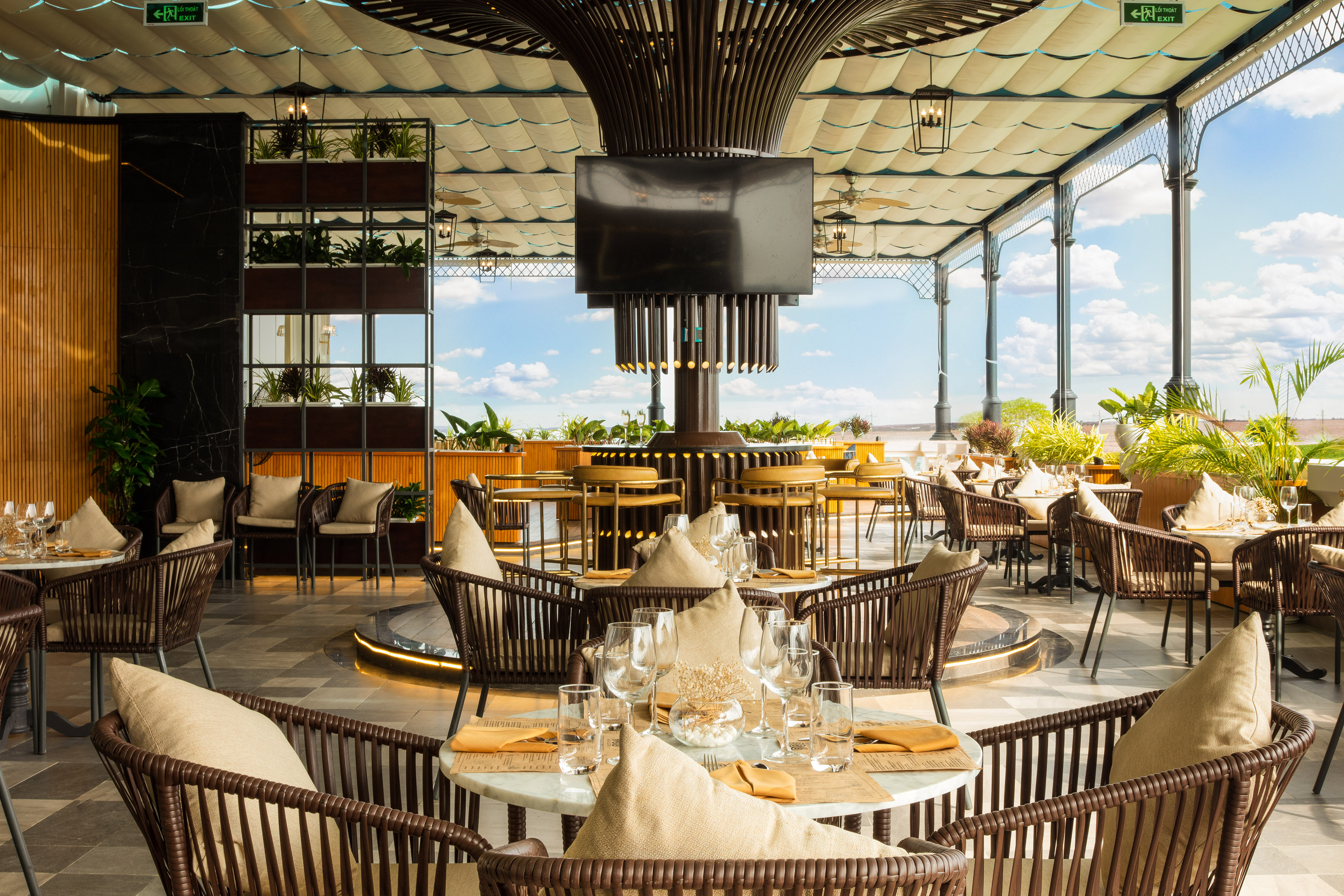 Luxury outdoor dining terrace with modern furniture, central bar, and greenery.