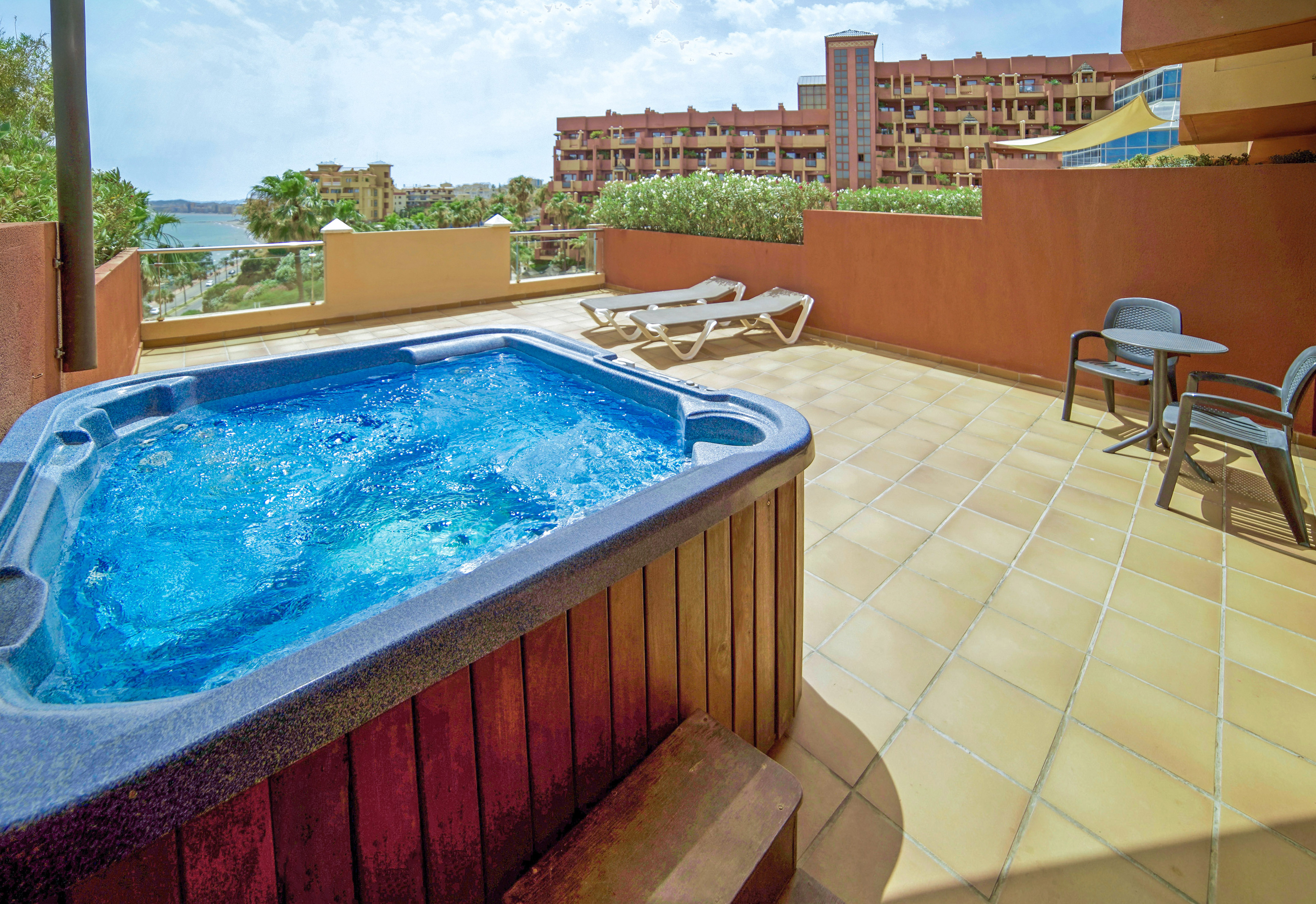 a hot tub on a patio with a deck chair and a building