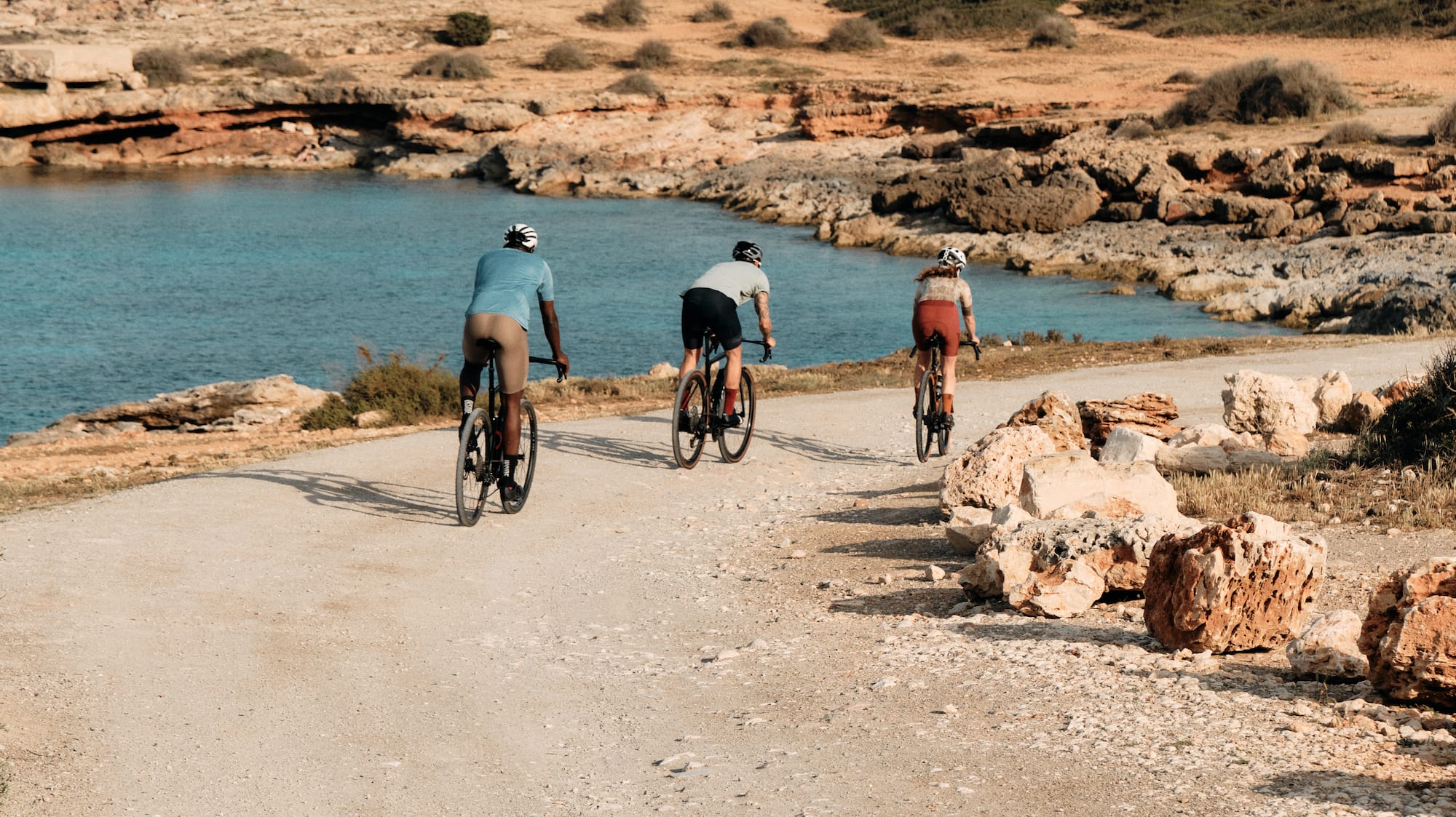 a group of people riding bikes on a dirt road near water