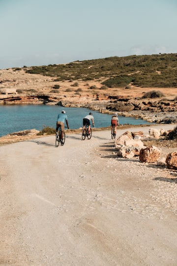 a group of people riding bikes on a dirt road near water