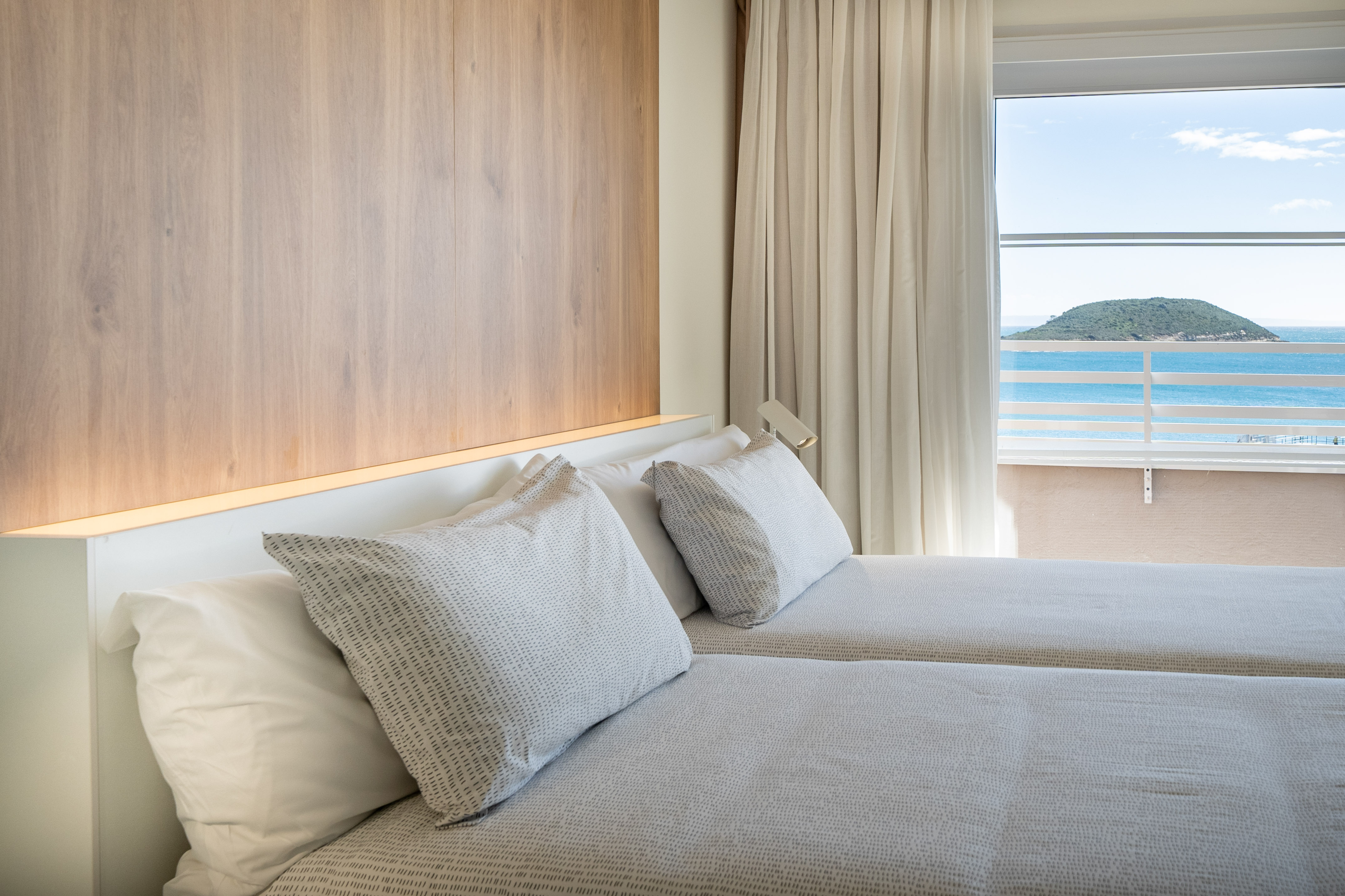 Modern hotel bedroom with twin beds and island sea view.