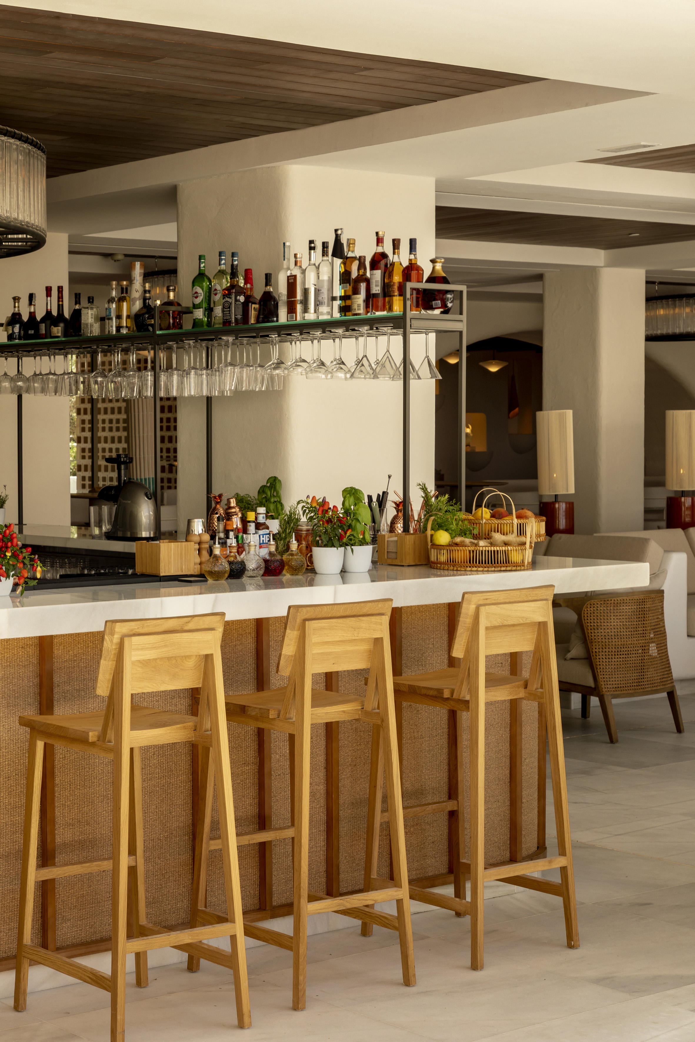 Hotel bar counter with liquor bottles, fresh fruits, and wooden stools.