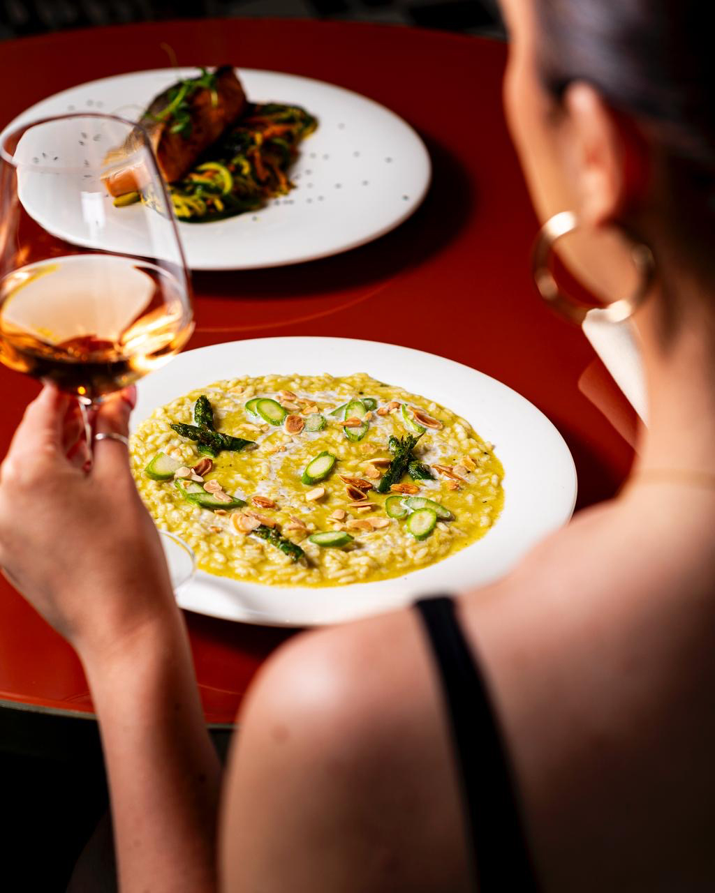Woman with rosé wine, creamy asparagus risotto, almonds, and salmon.