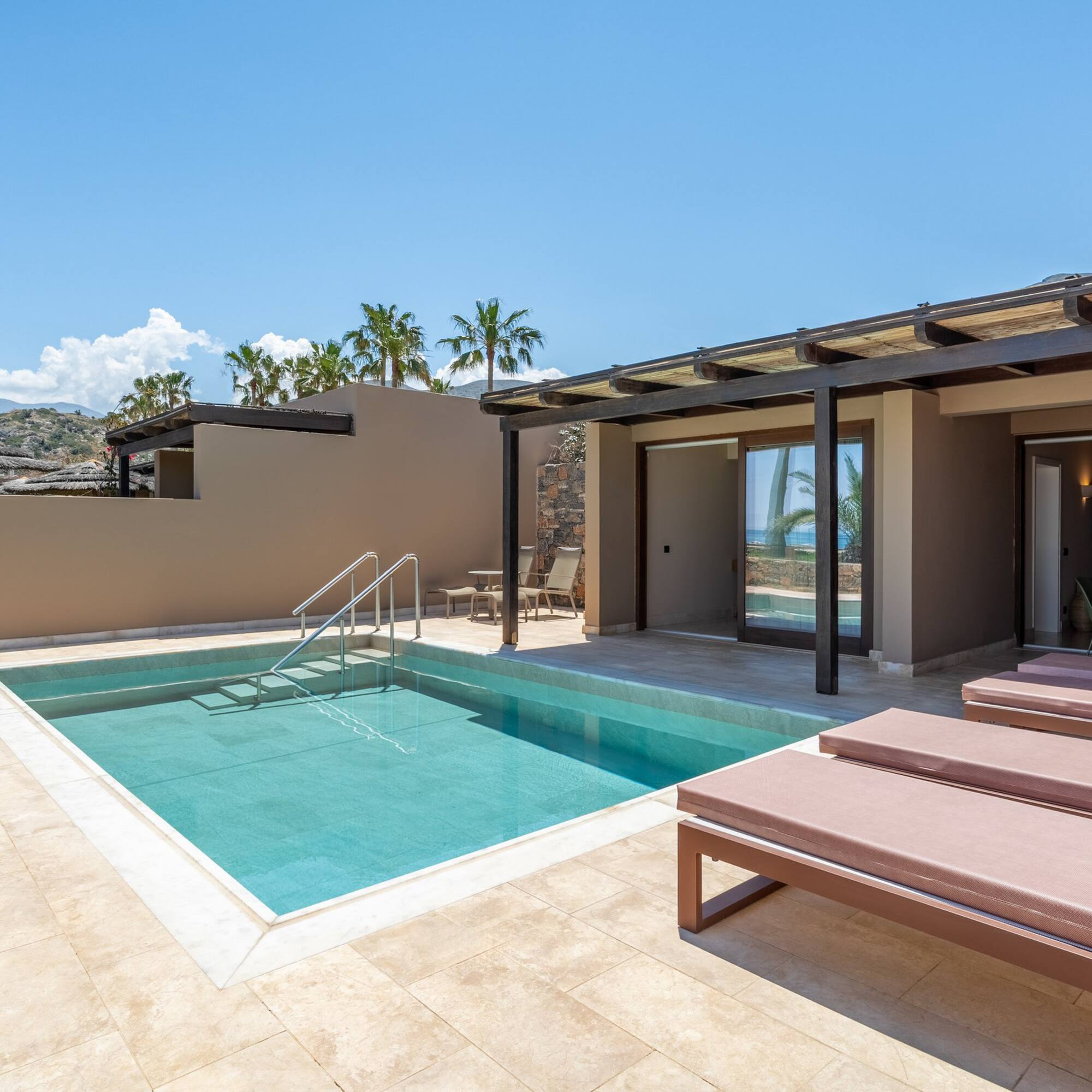 Modern hotel suite with private pool, sunbeds, and ocean view patio.