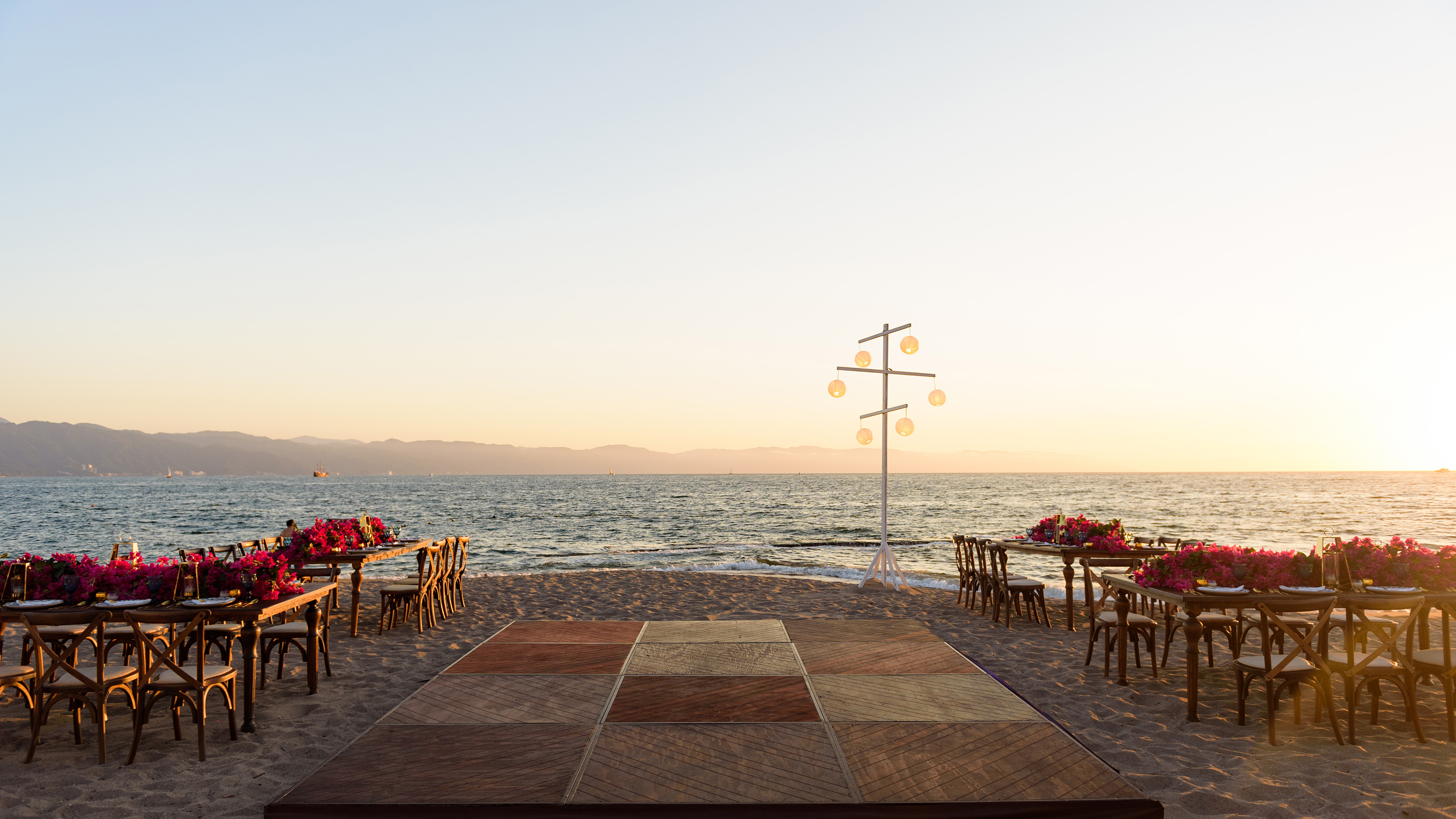 Sunset beach wedding reception with floral tables, dance floor, and ocean.