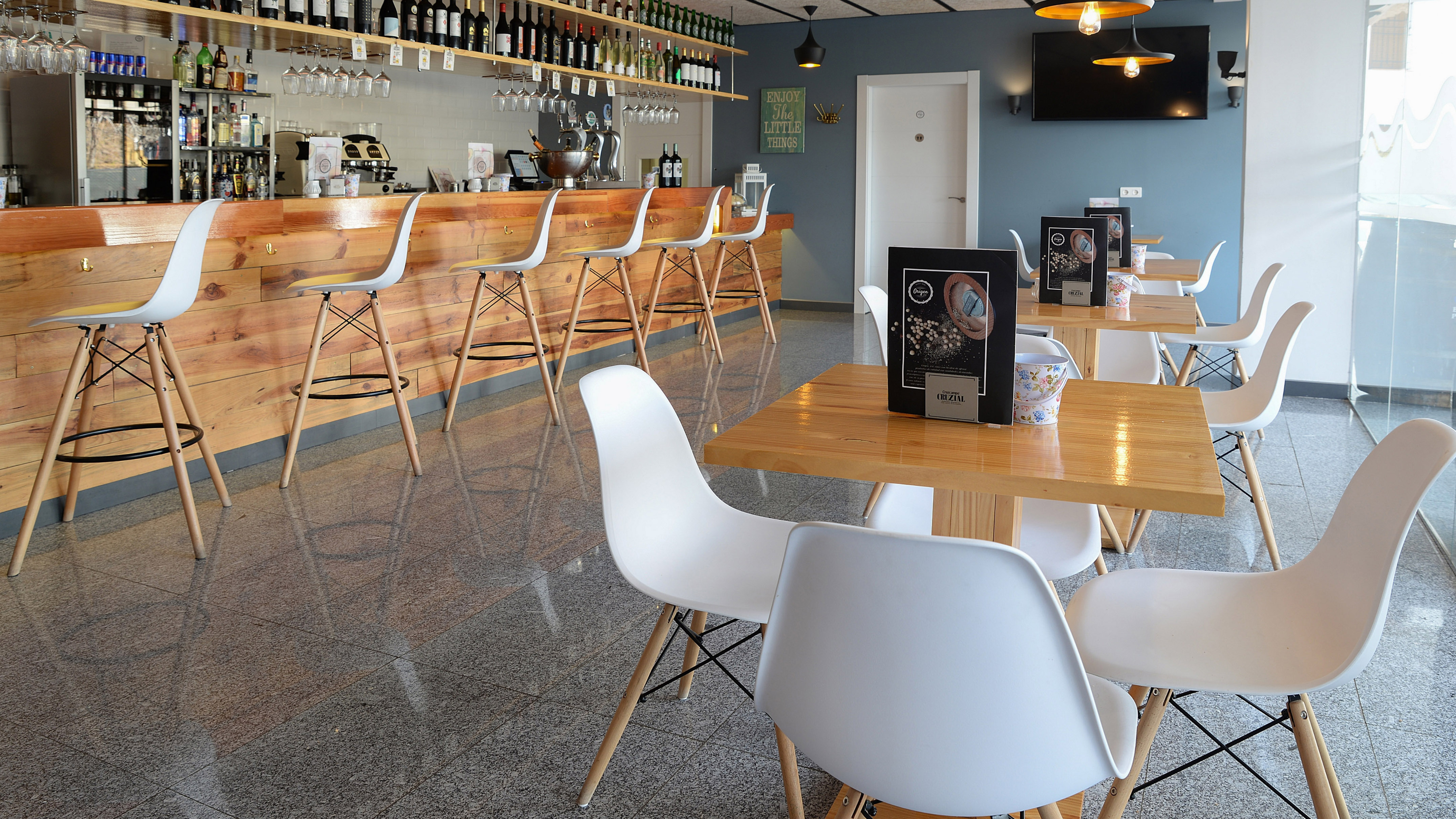 Modern bar and cafe interior with wooden counter, white stools, tables, and chairs.