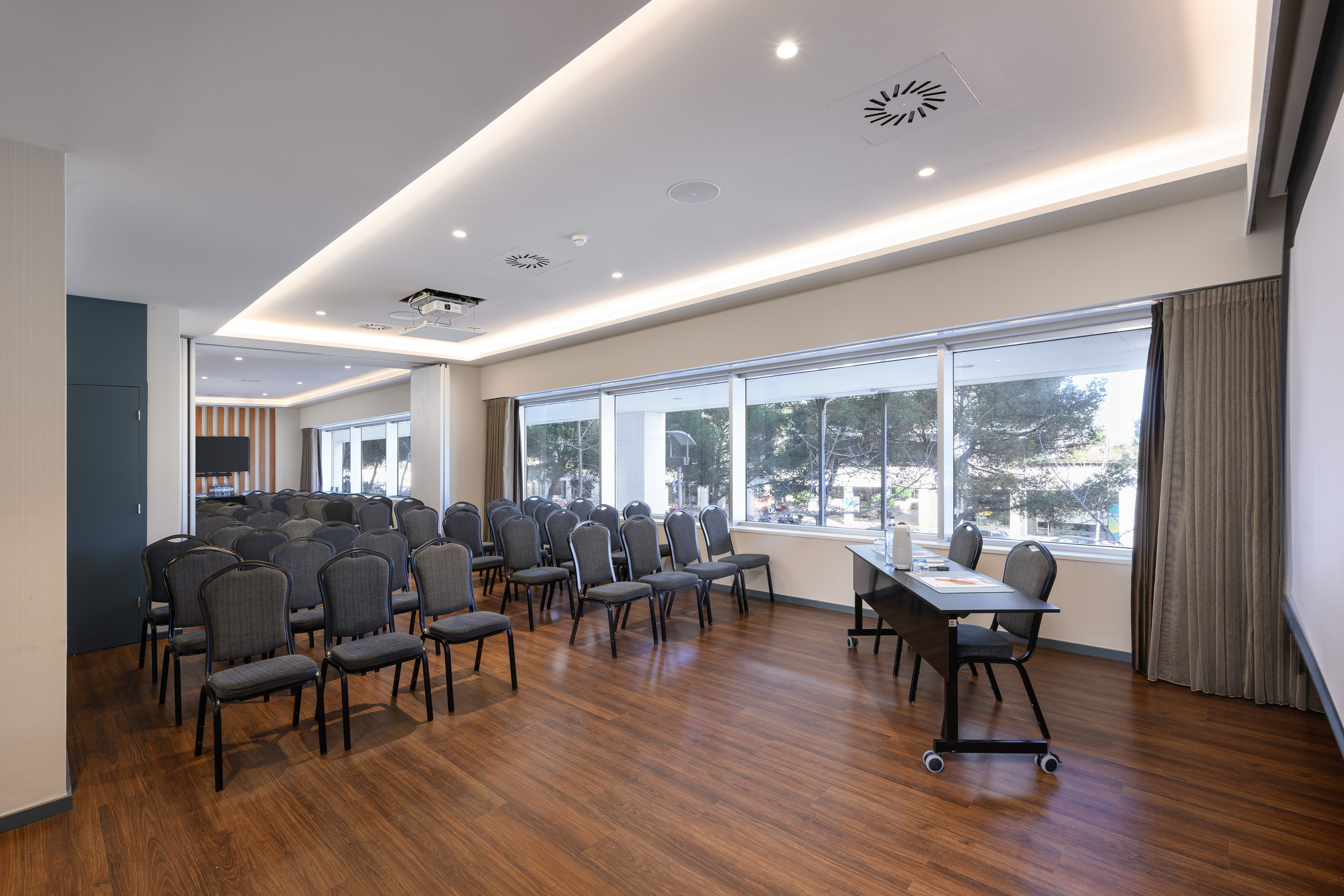 Modern meeting room with chairs, presentation table, projector, and large windows.