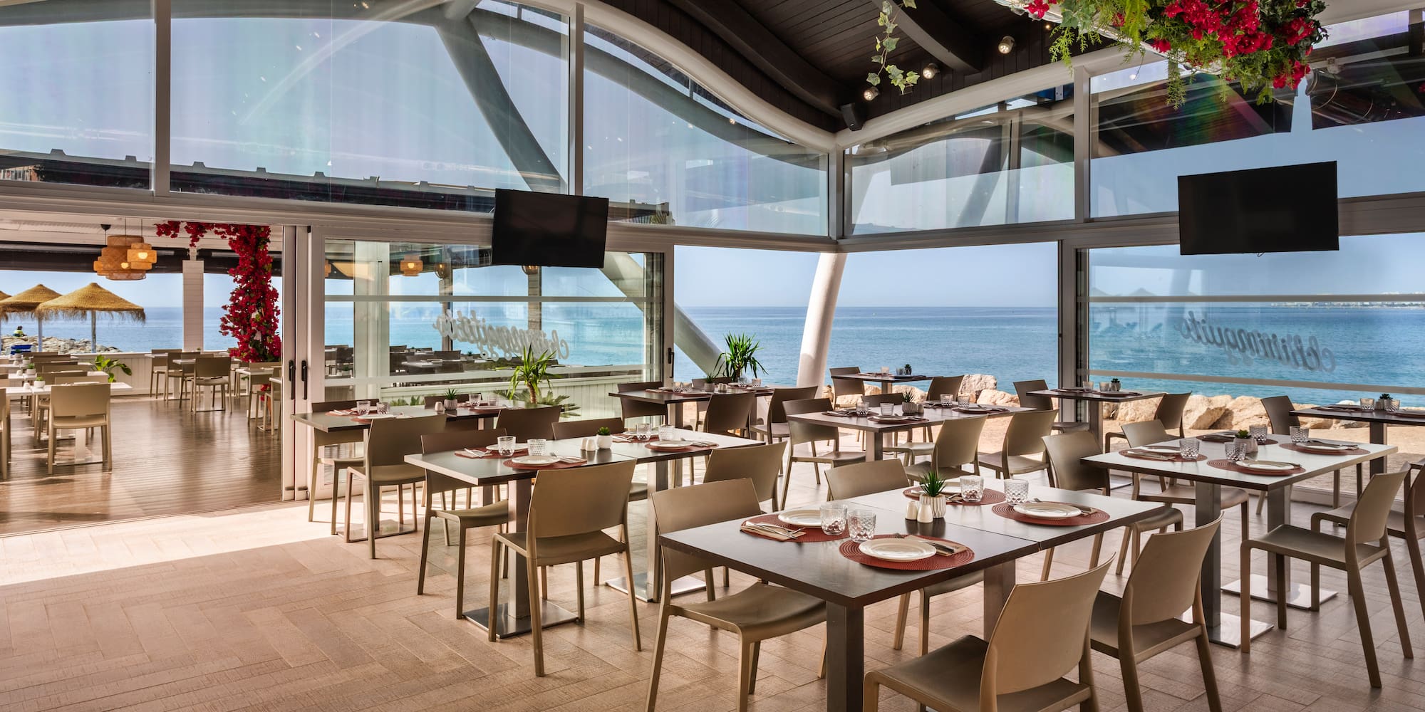 Beachfront restaurant with ocean views, set tables, and red floral decor.