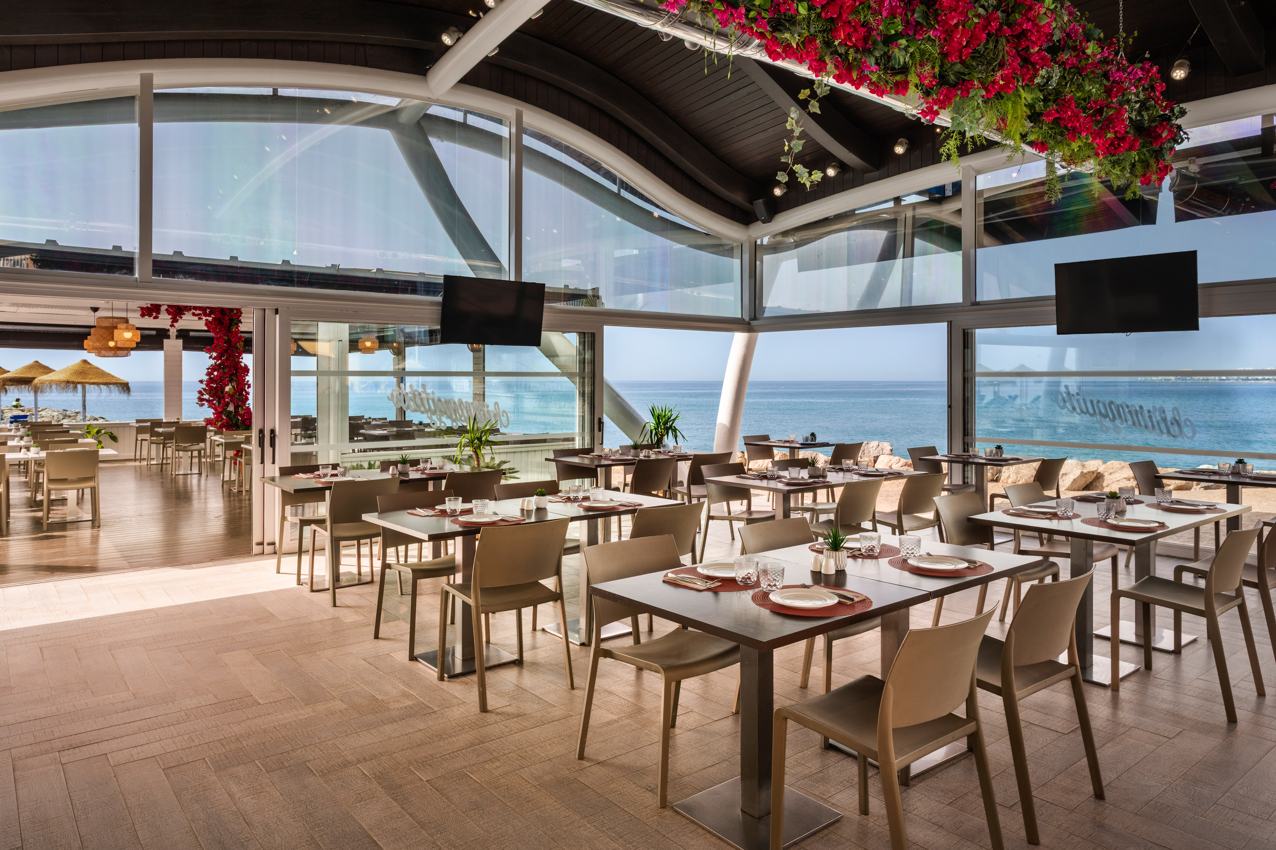Beachfront restaurant with ocean views, set tables, and red floral decor.
