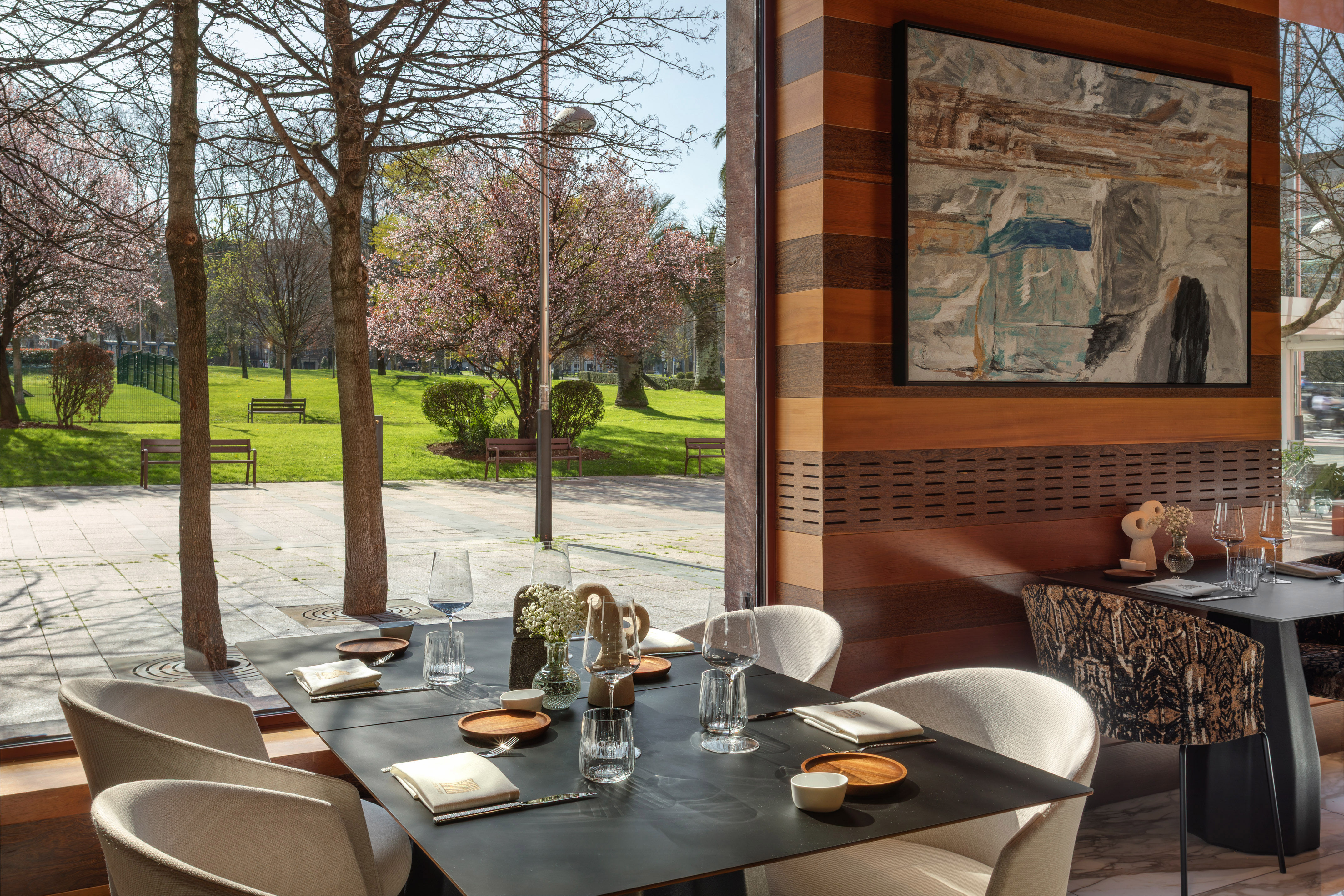Modern restaurant dining table by window, with park view and cherry blossoms.