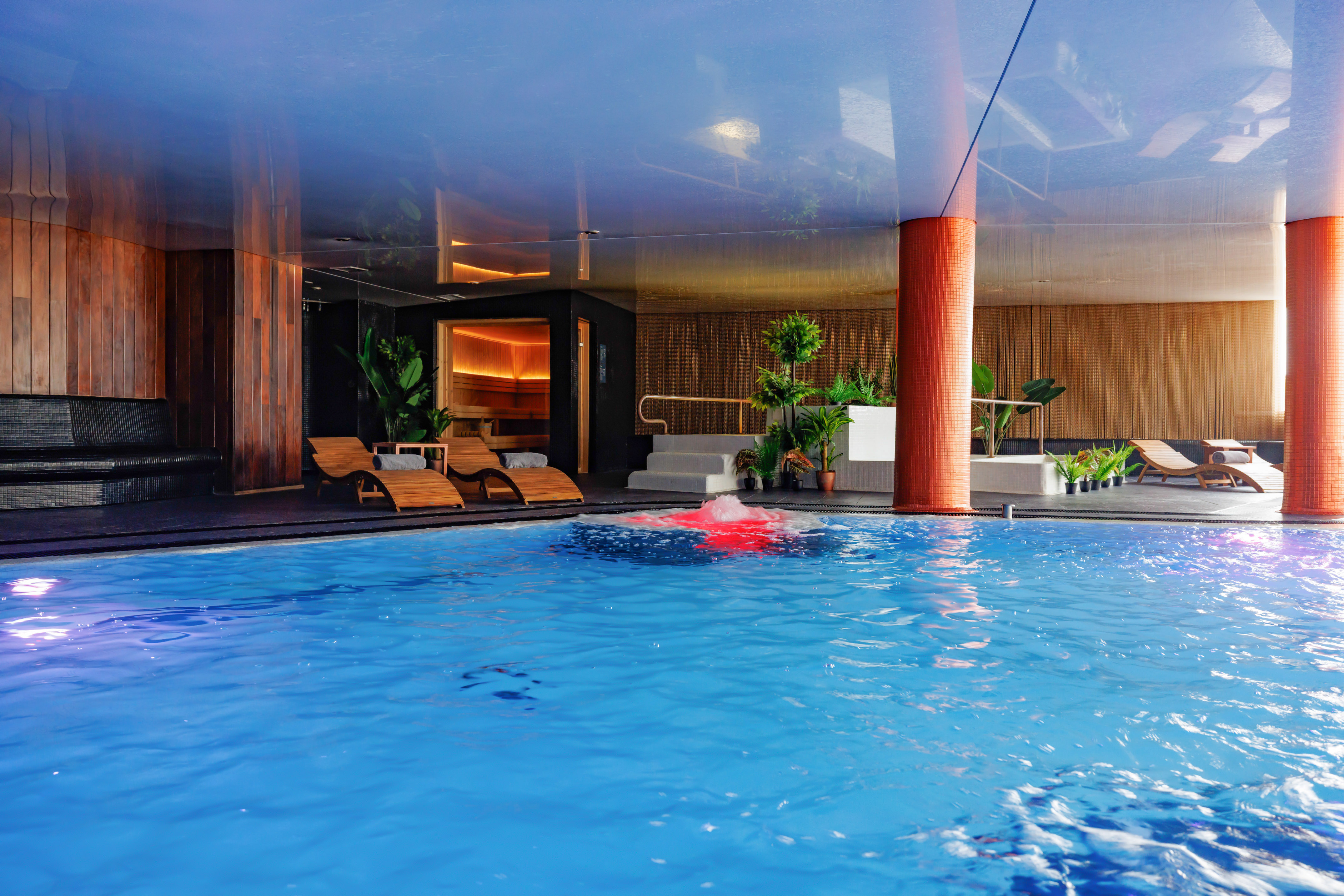 Modern indoor spa pool, sauna, and wooden loungers for relaxation.