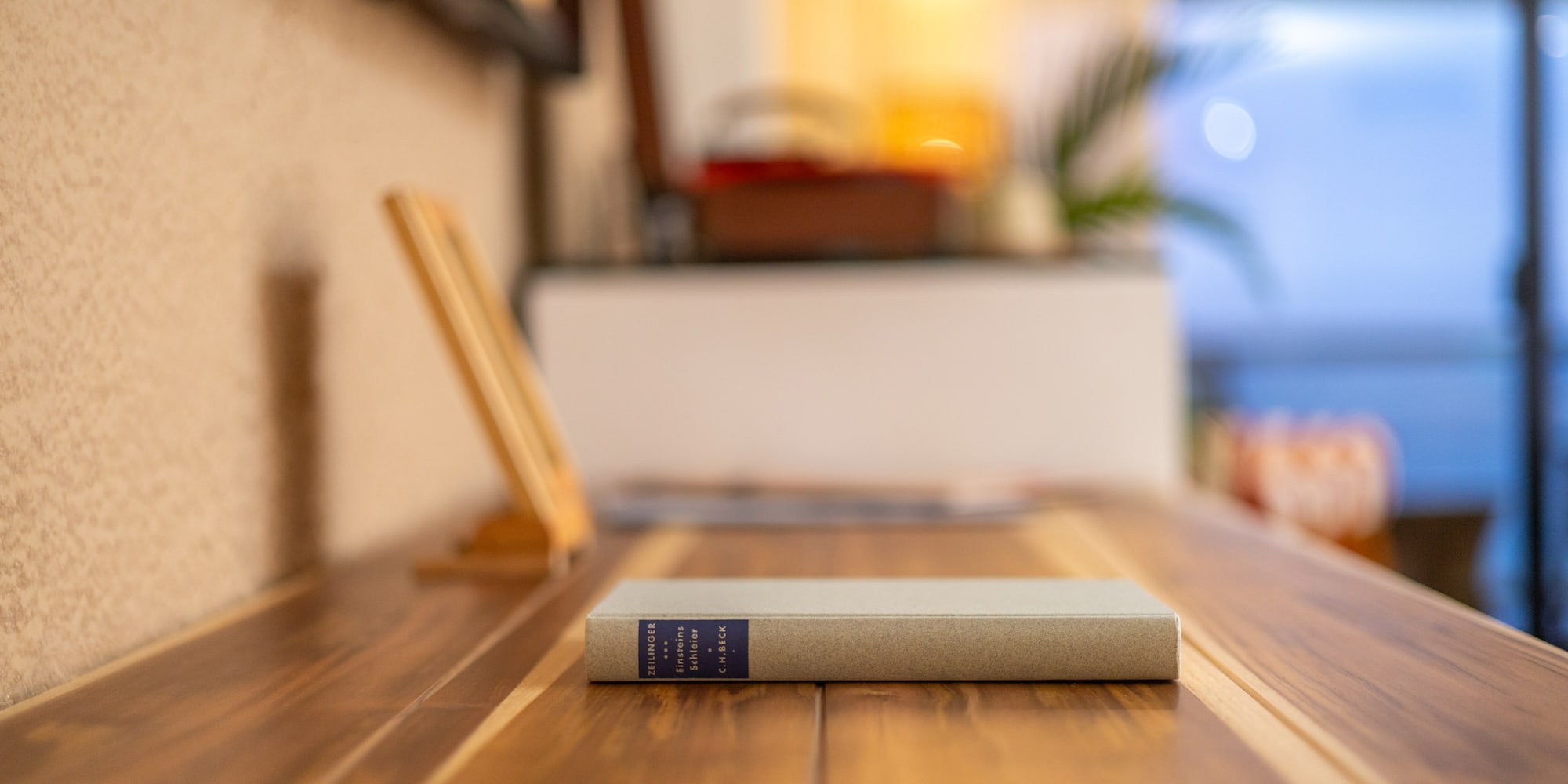 Libro de Zeilinger "Einsteins Schleier" sobre mesa de madera en interior acogedor.
