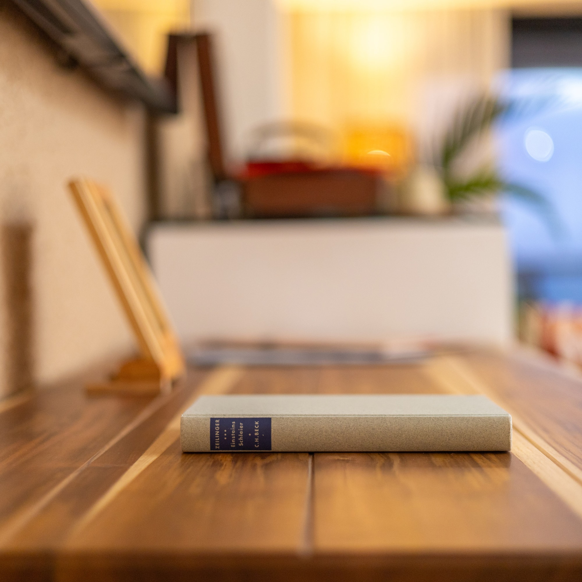Light book "Einsteins Schleier" by Zeilinger on a wooden desk.