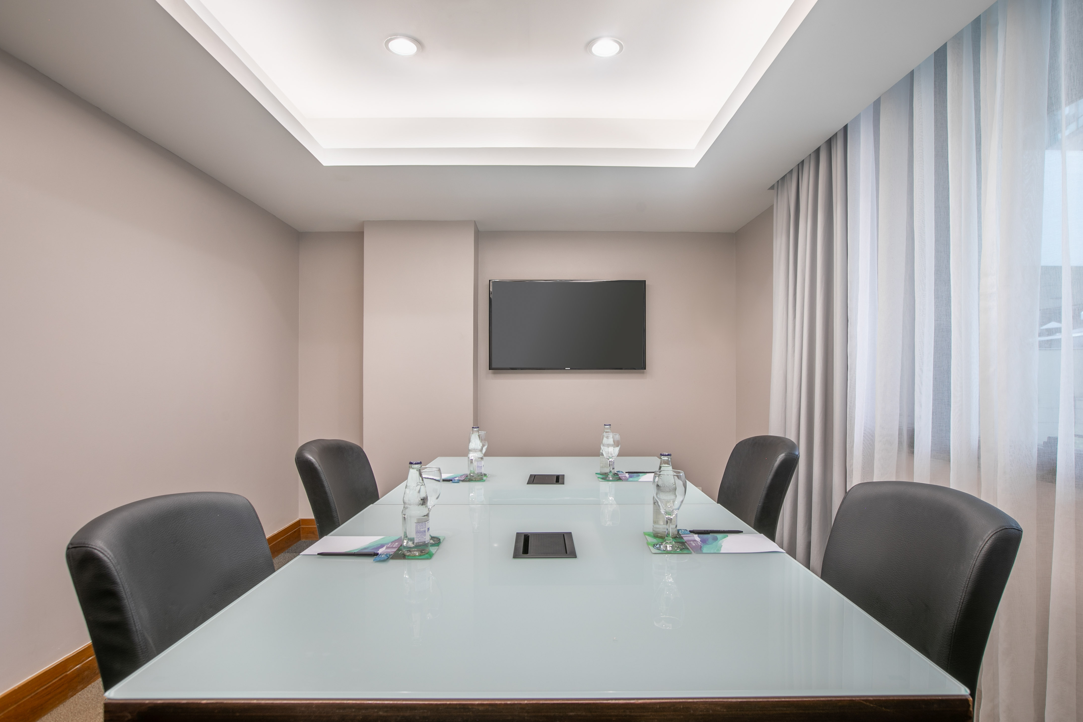 Modern meeting room with long conference table, chairs, and wall-mounted screen.